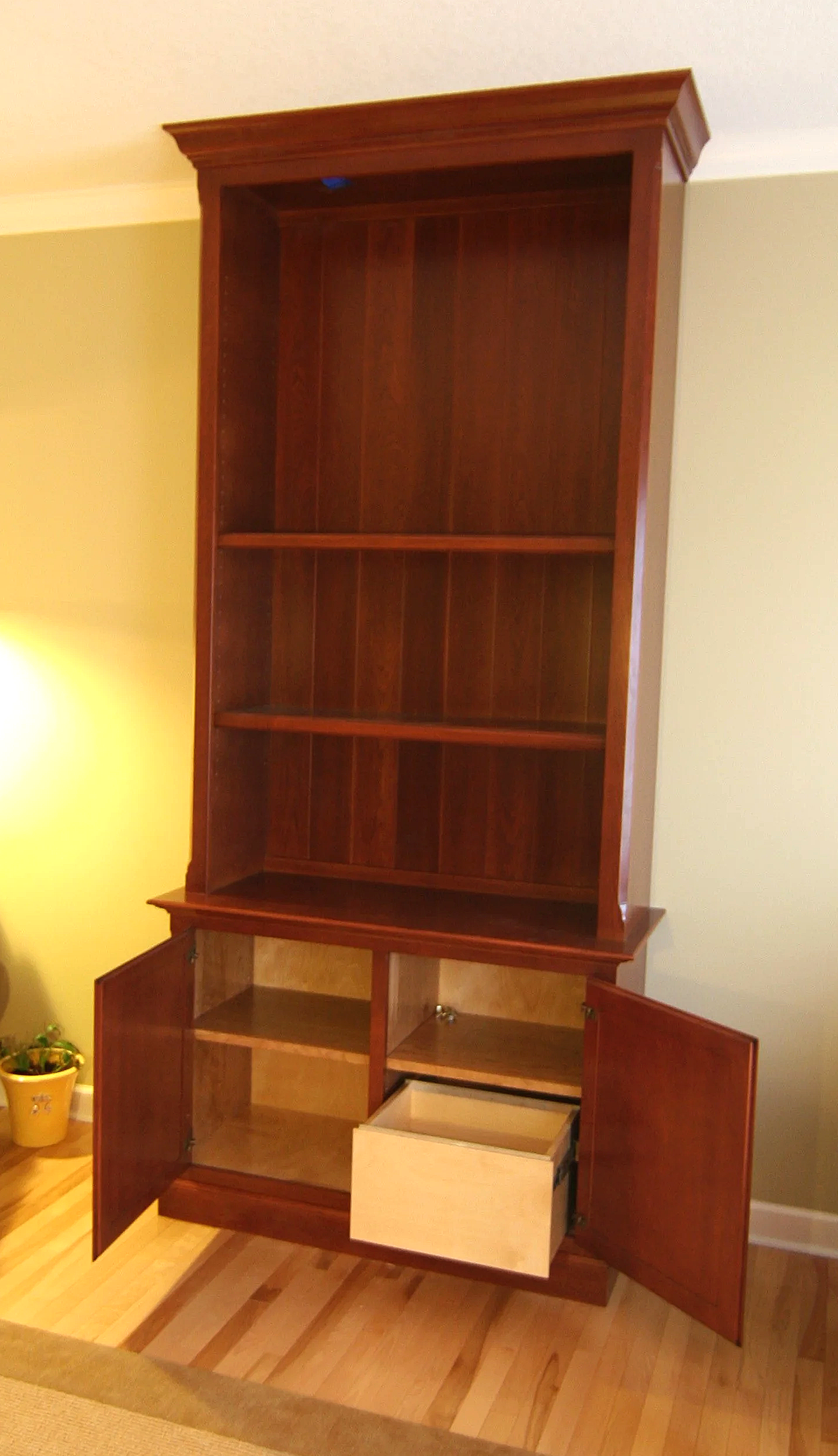 Empty wooden bookshelf with doors open, revealing shelves and a drawer inside.