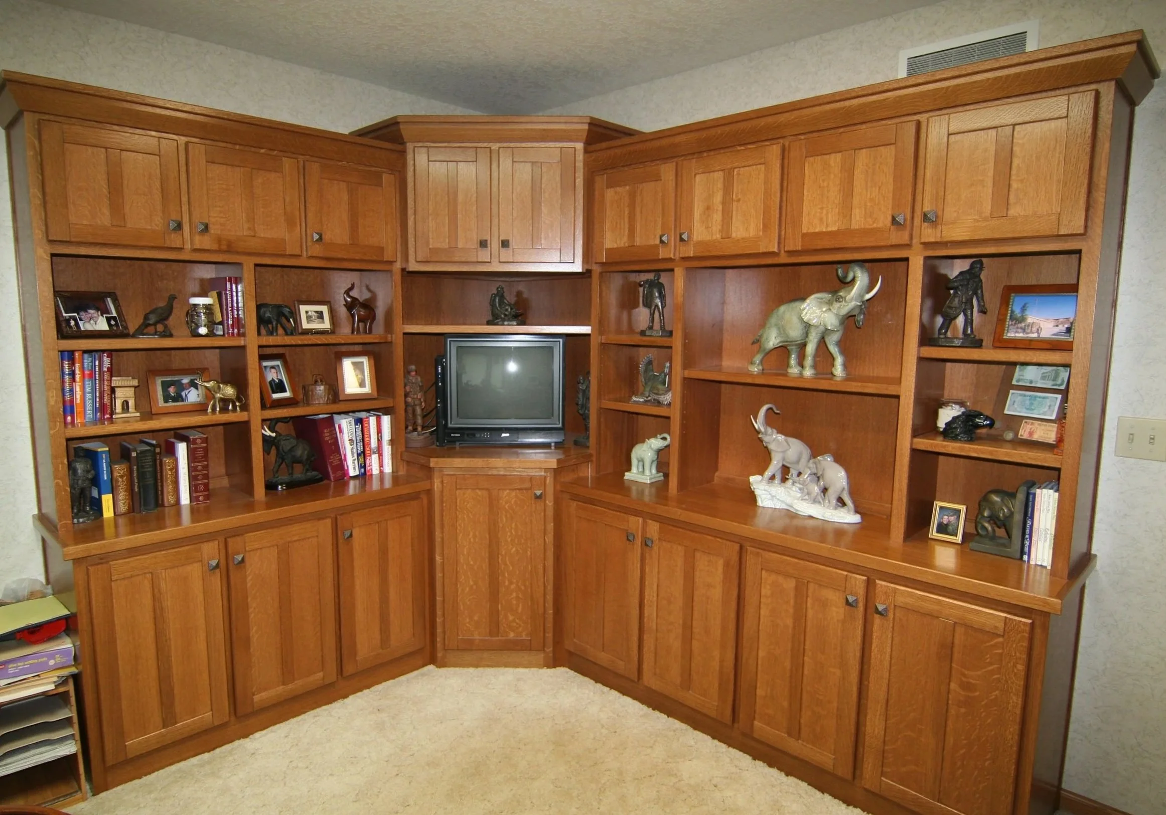 Wooden living room wall unit with shelves filled with books and animal figurines, a small CRT TV in the center, and a beige carpeted floor.