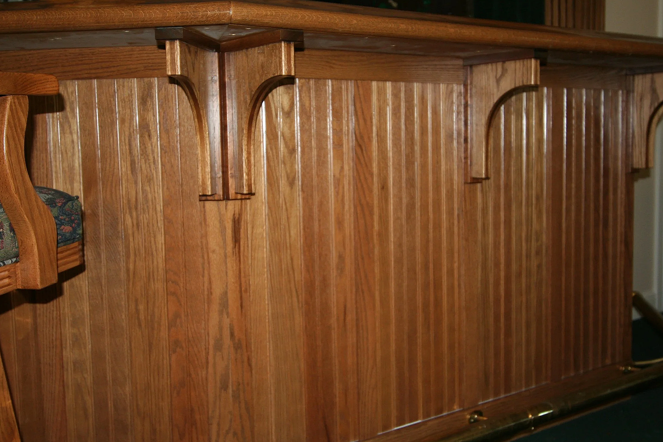 Close-up of a wooden church pew with vertical slats on the side and a floral cushion on the seat.