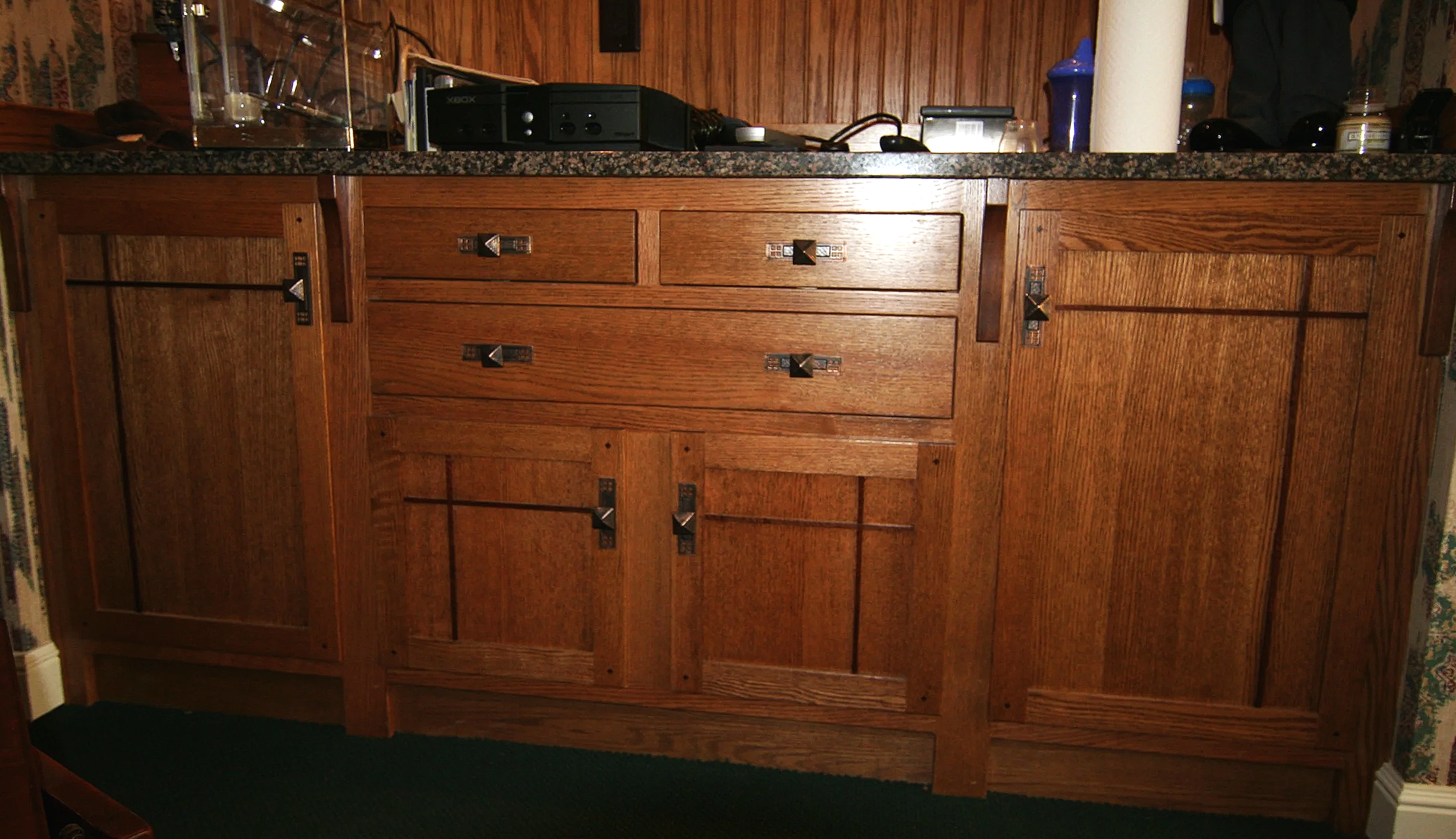 Wooden kitchen cabinet with granite countertop, various kitchen items, and a black electronic device on top.