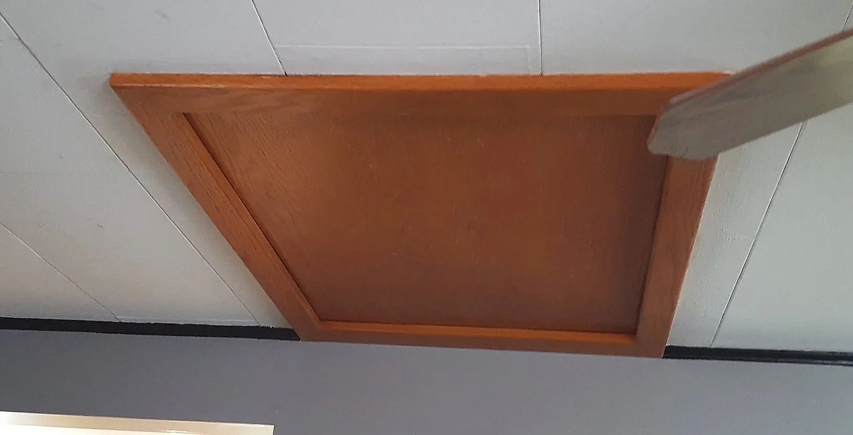 A wooden square panel on a tiled wall with a part of a rounded-edged mirror or frame visible to the right.