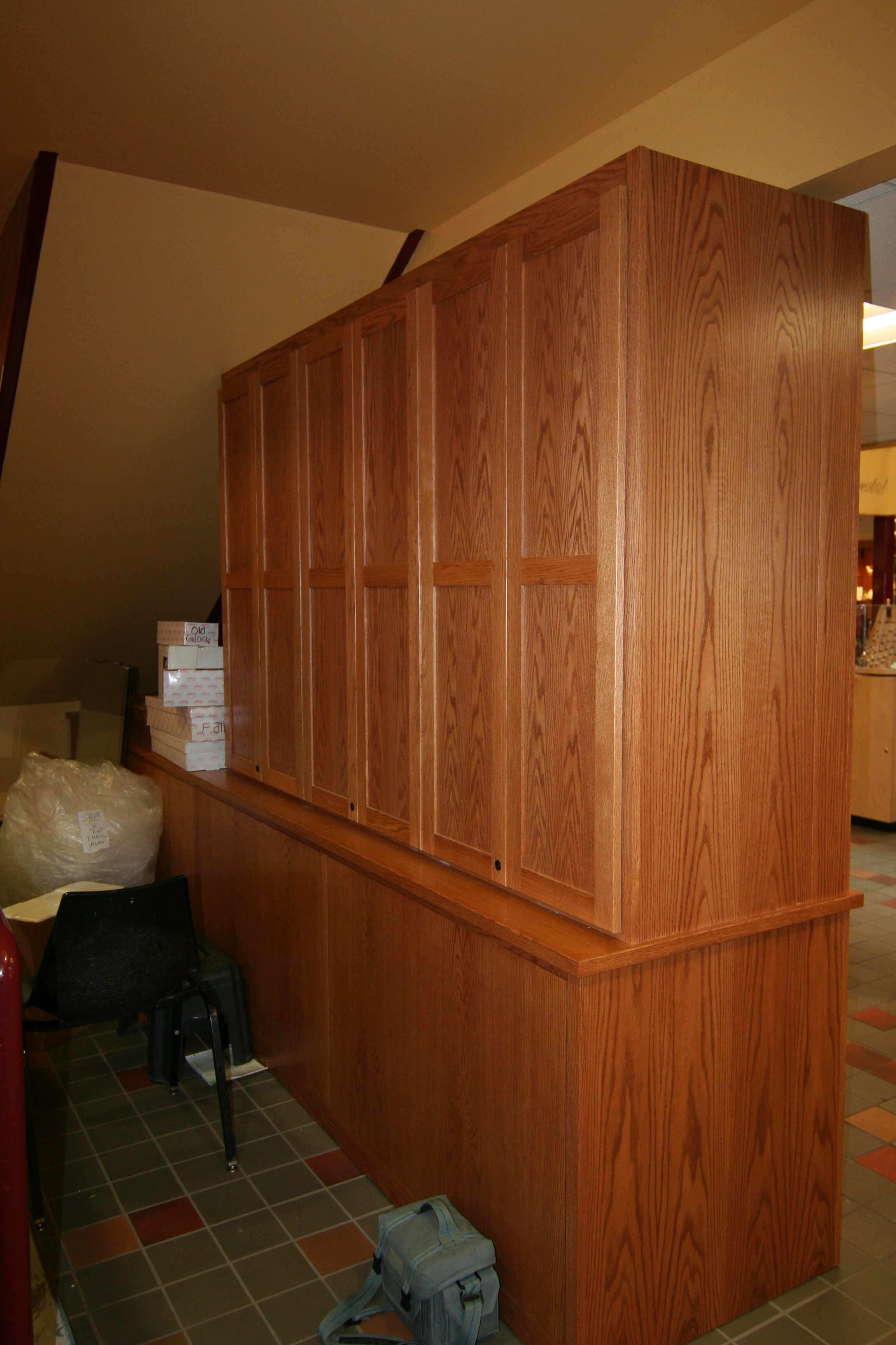 Tall wooden partition with vertical panels in a room, adjacent to a counter and chairs, with a tiled floor.