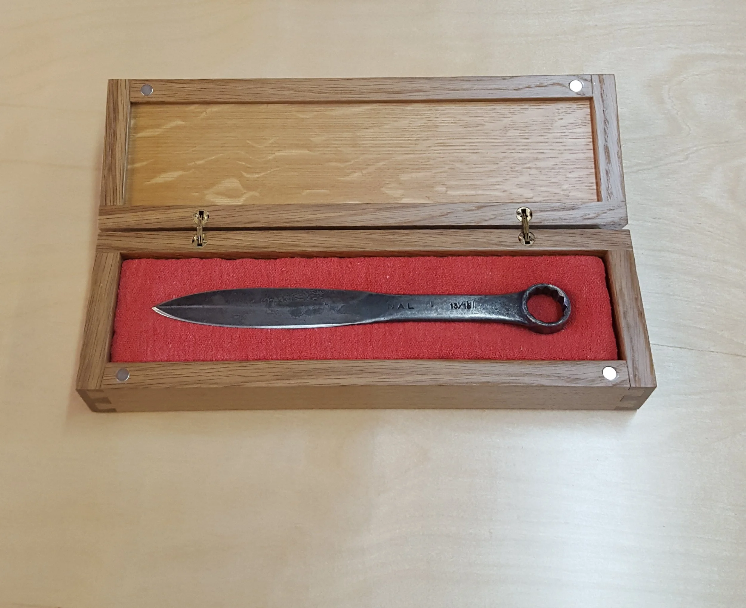 A metal tool with a round hole at one end, placed inside a wooden display box with a red velvet lining.