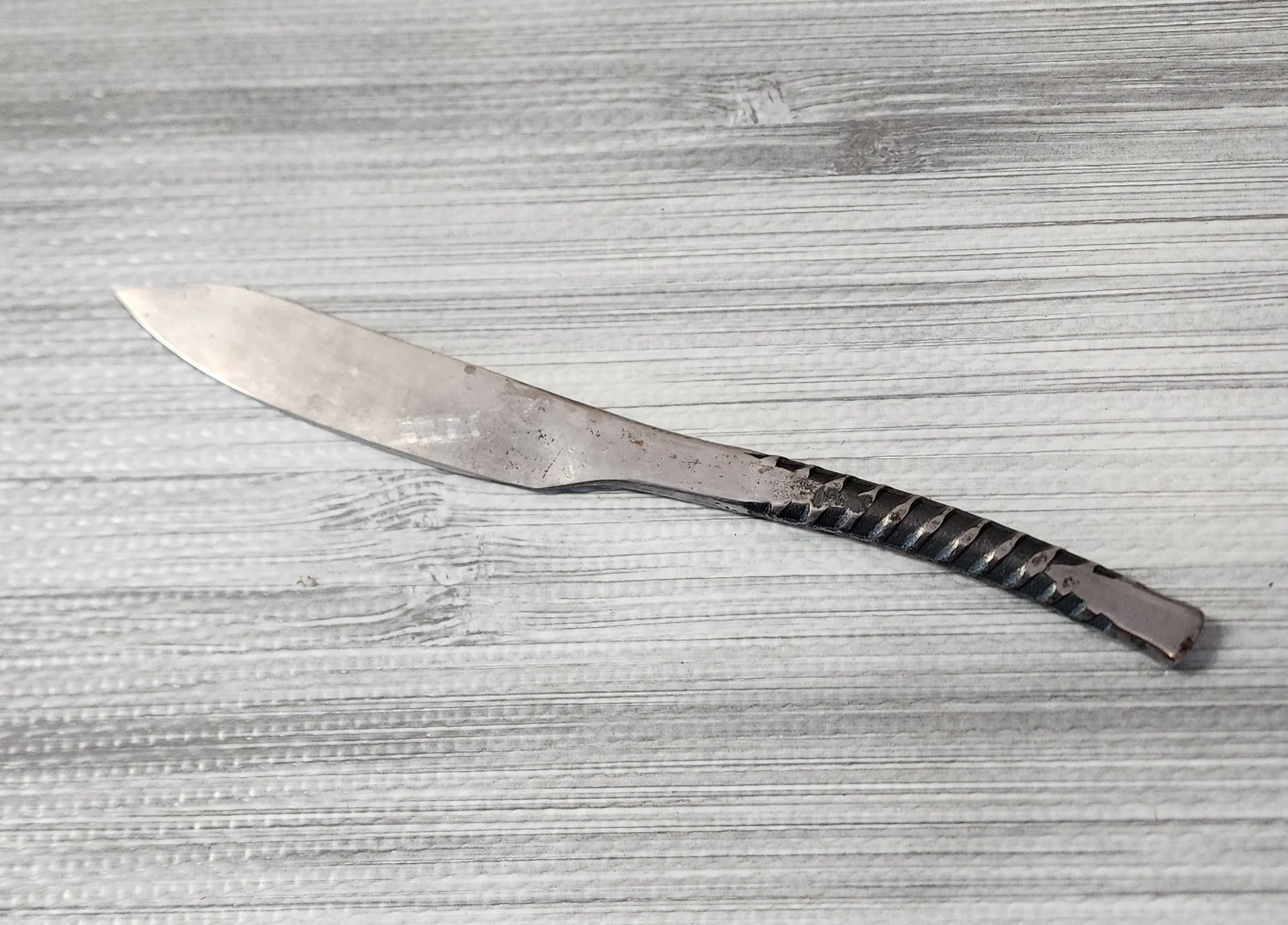 A steel butter knife with a textured handle lying on a wooden surface.