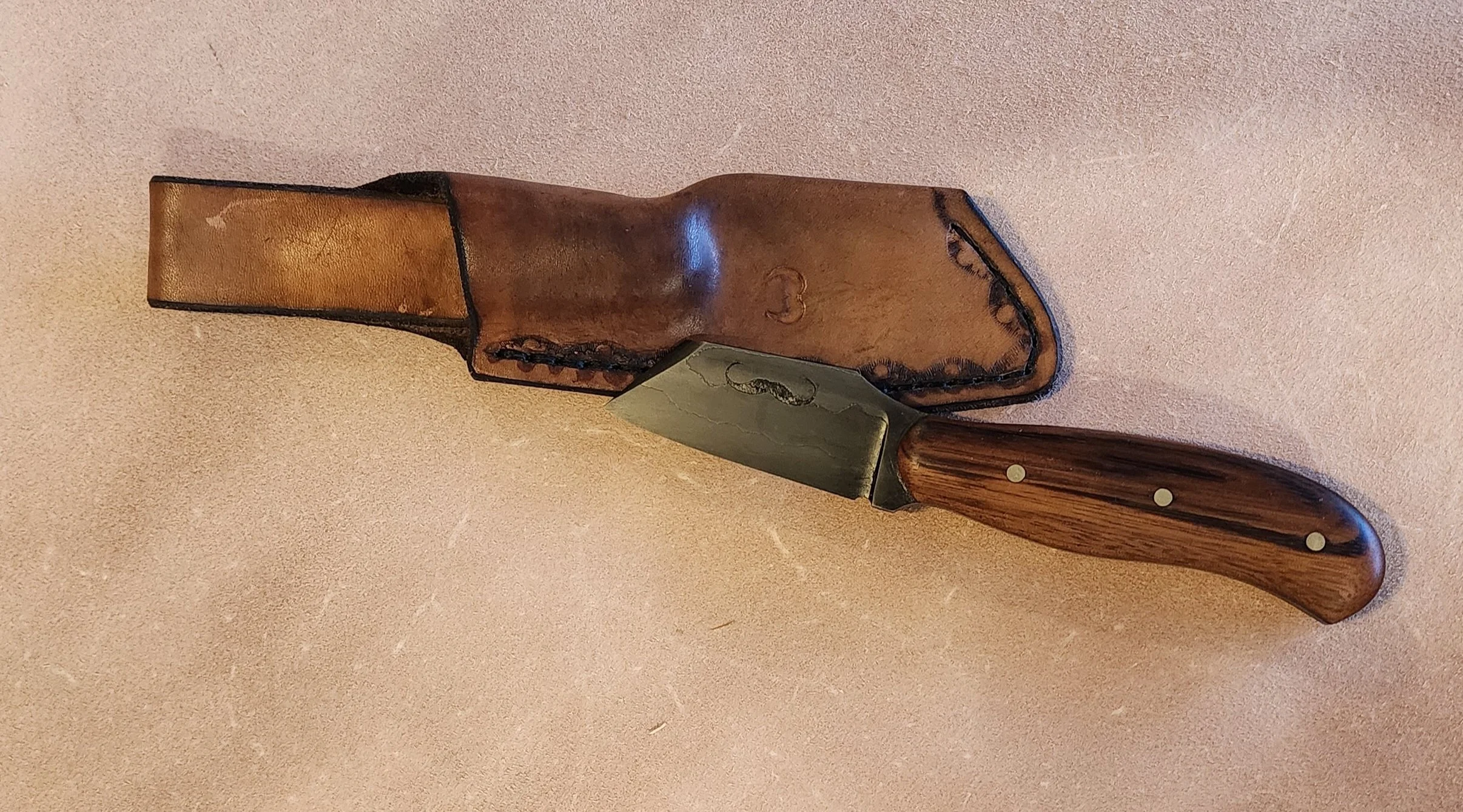 A fixed-blade knife with a wooden handle and a curved blade, accompanied by a brown leather sheath.
