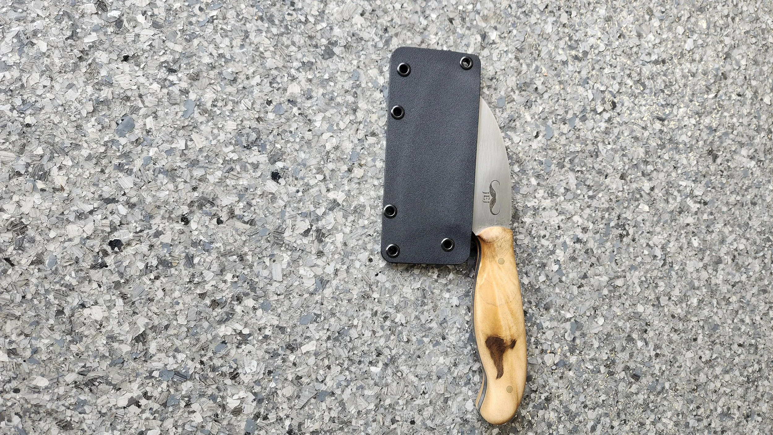 A small knife with a light-colored wooden handle and a stainless steel blade resting on a speckled gray surface.