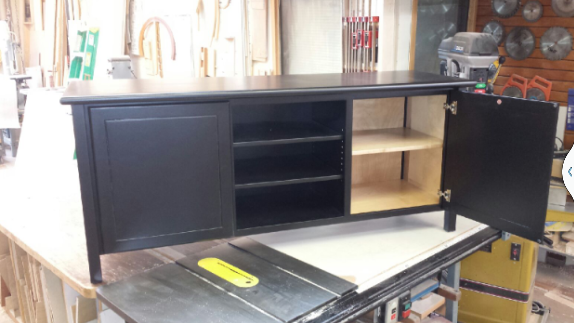 Black wooden sideboard with open and closed storage compartments in a woodworking workshop.