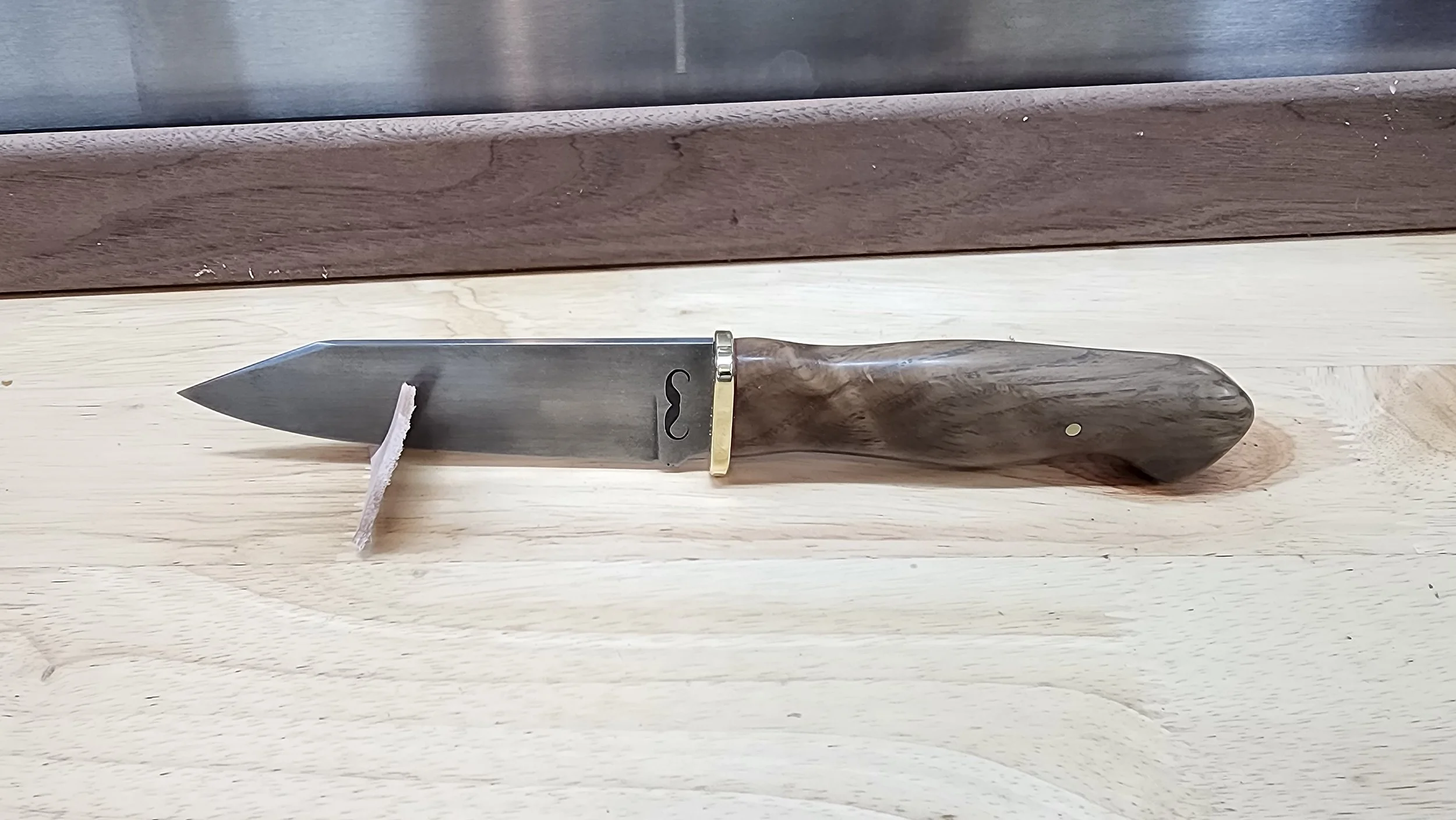 A kitchen knife with a dark wooden handle and a large silver blade, resting on a light-colored wooden surface.