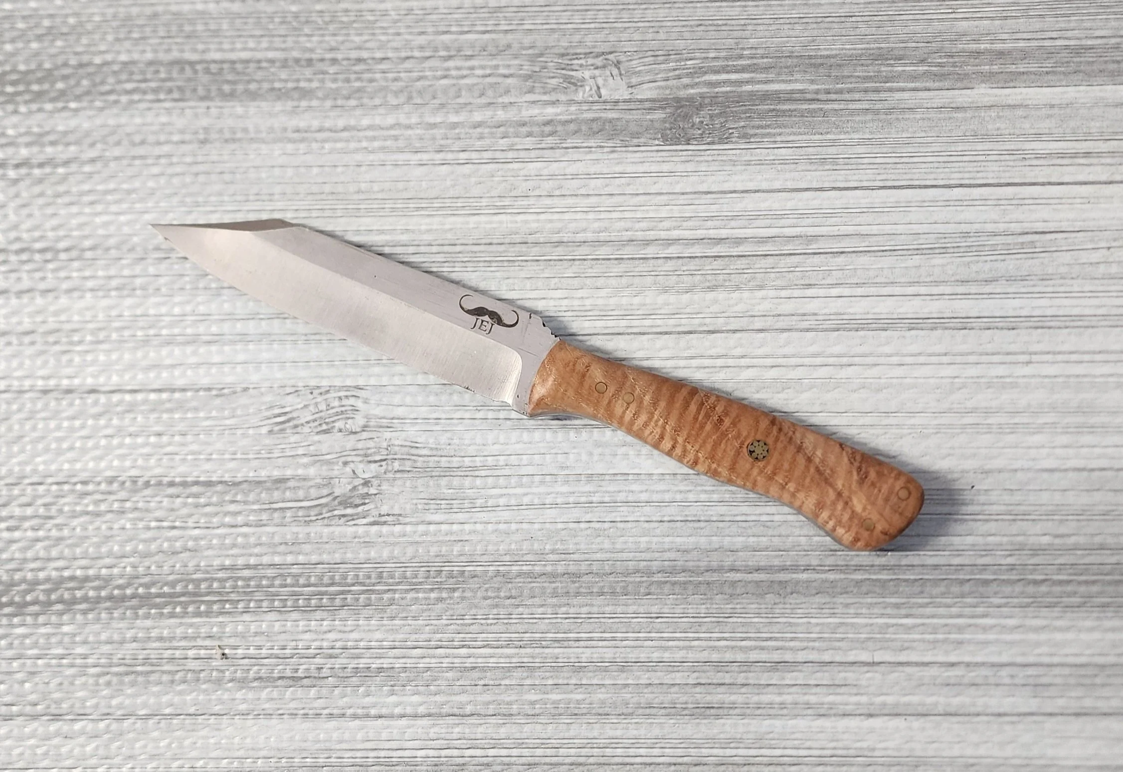 A small kitchen knife with a wooden handle lying on a textured gray surface.