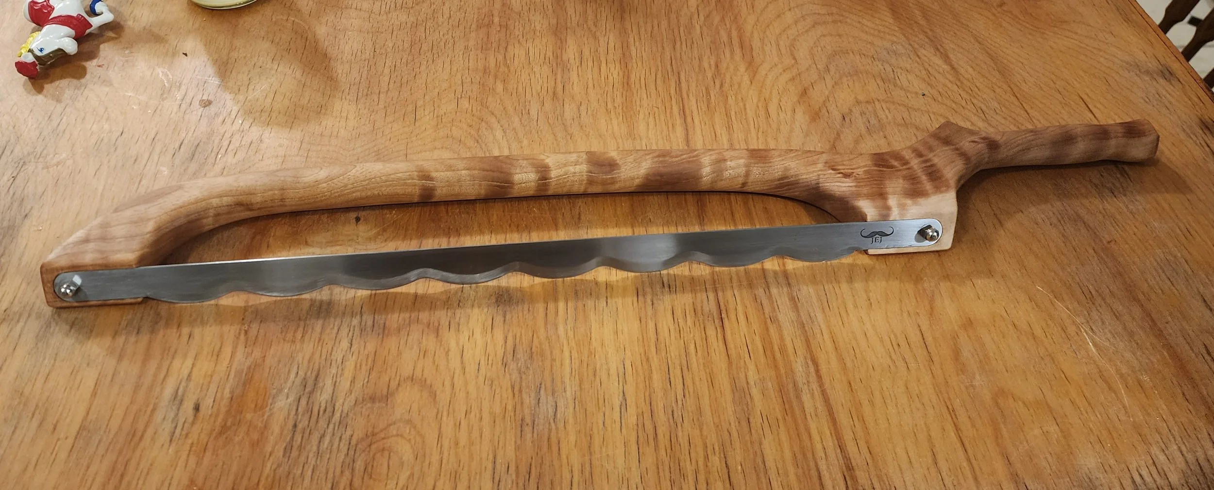 A butter knife with a wooden handle and a serrated stainless steel blade resting on a wooden table.