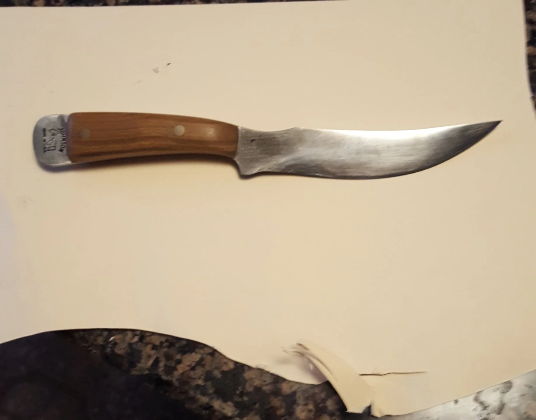 A small curved kitchen or butcher knife with a wooden handle and a slightly worn metal blade rests on a beige surface.