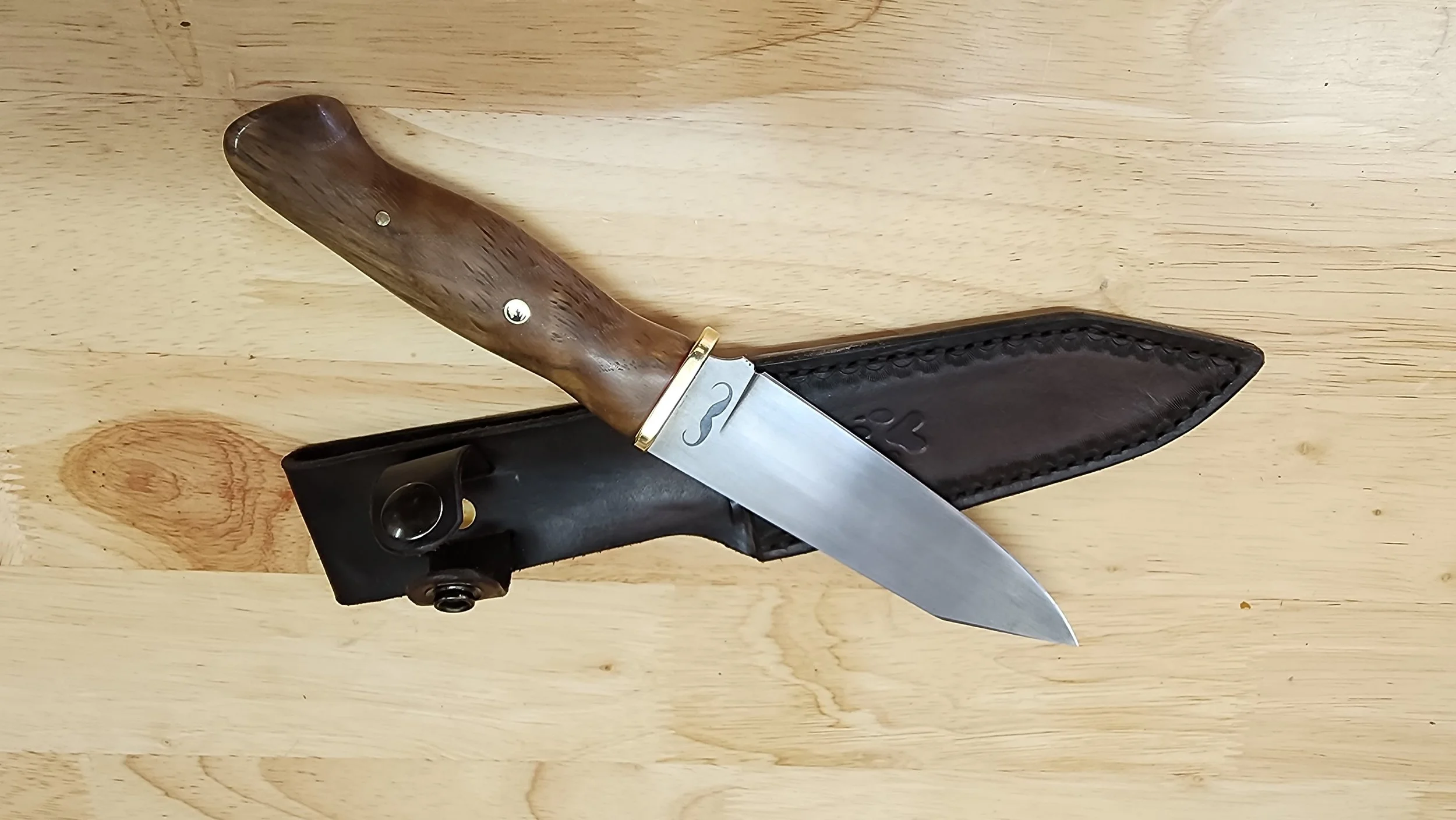 A pocket knife with a wood handle, partially opened, resting on a black leather sheath on a wooden surface.