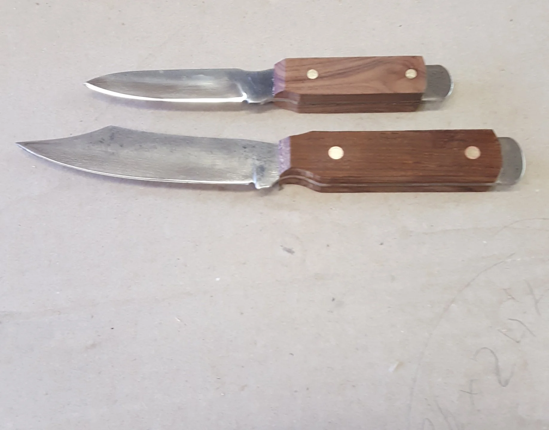 Two knives with wooden handles placed on a light-colored surface.