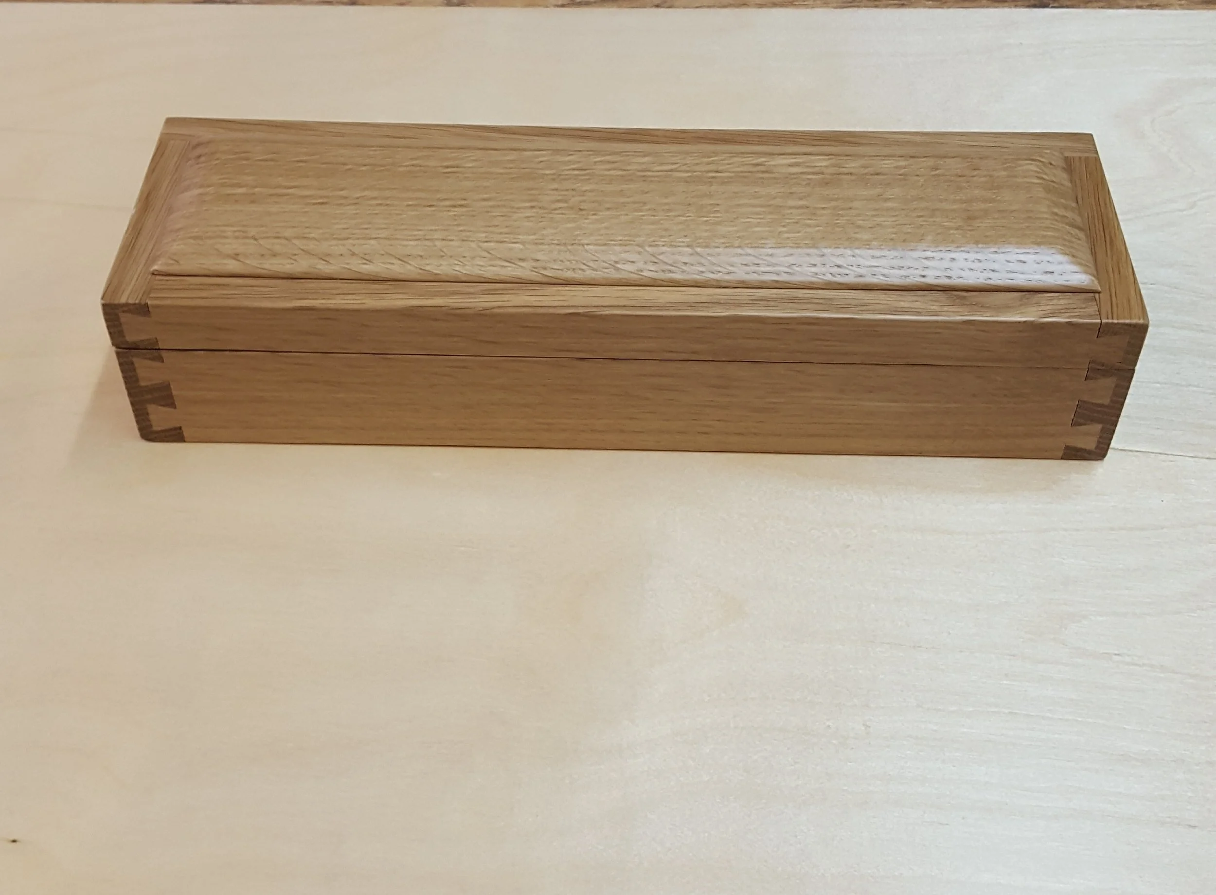 A rectangular wooden box with dovetail joints on the corners, resting on a light-colored wooden surface.