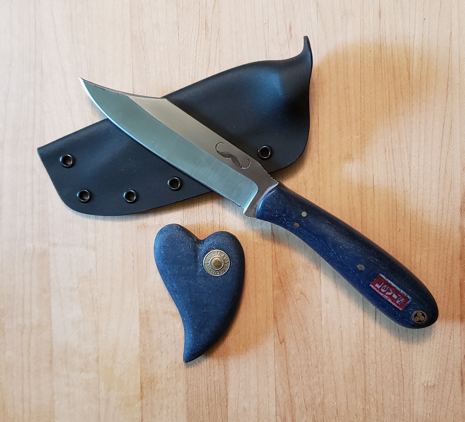 A kitchen knife with a wooden handle, a black sheath with rivets, and a sharpening stone.