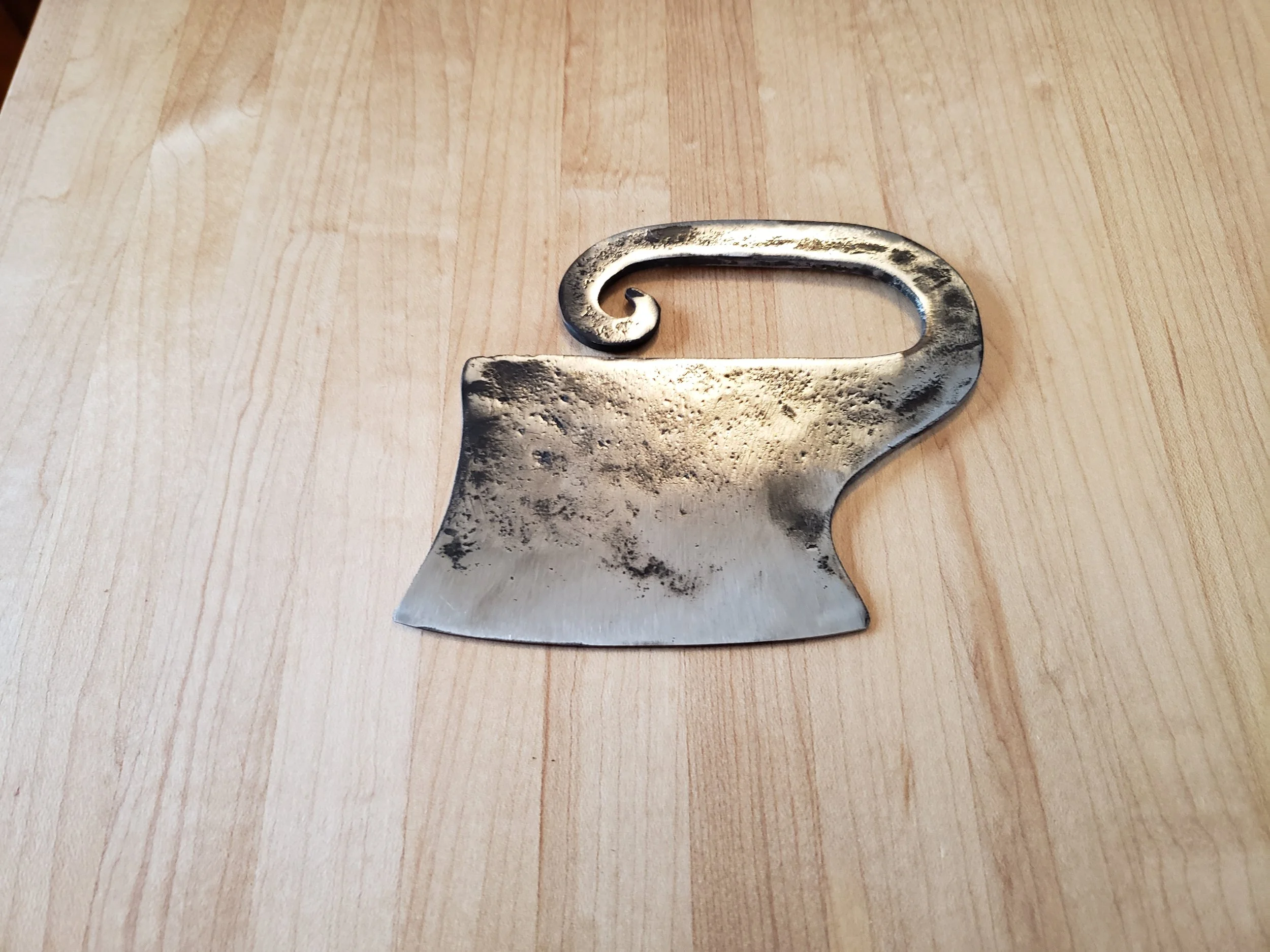 A vintage metal cheese cutter with a curved handle and a wide flat blade, resting on a wooden surface.