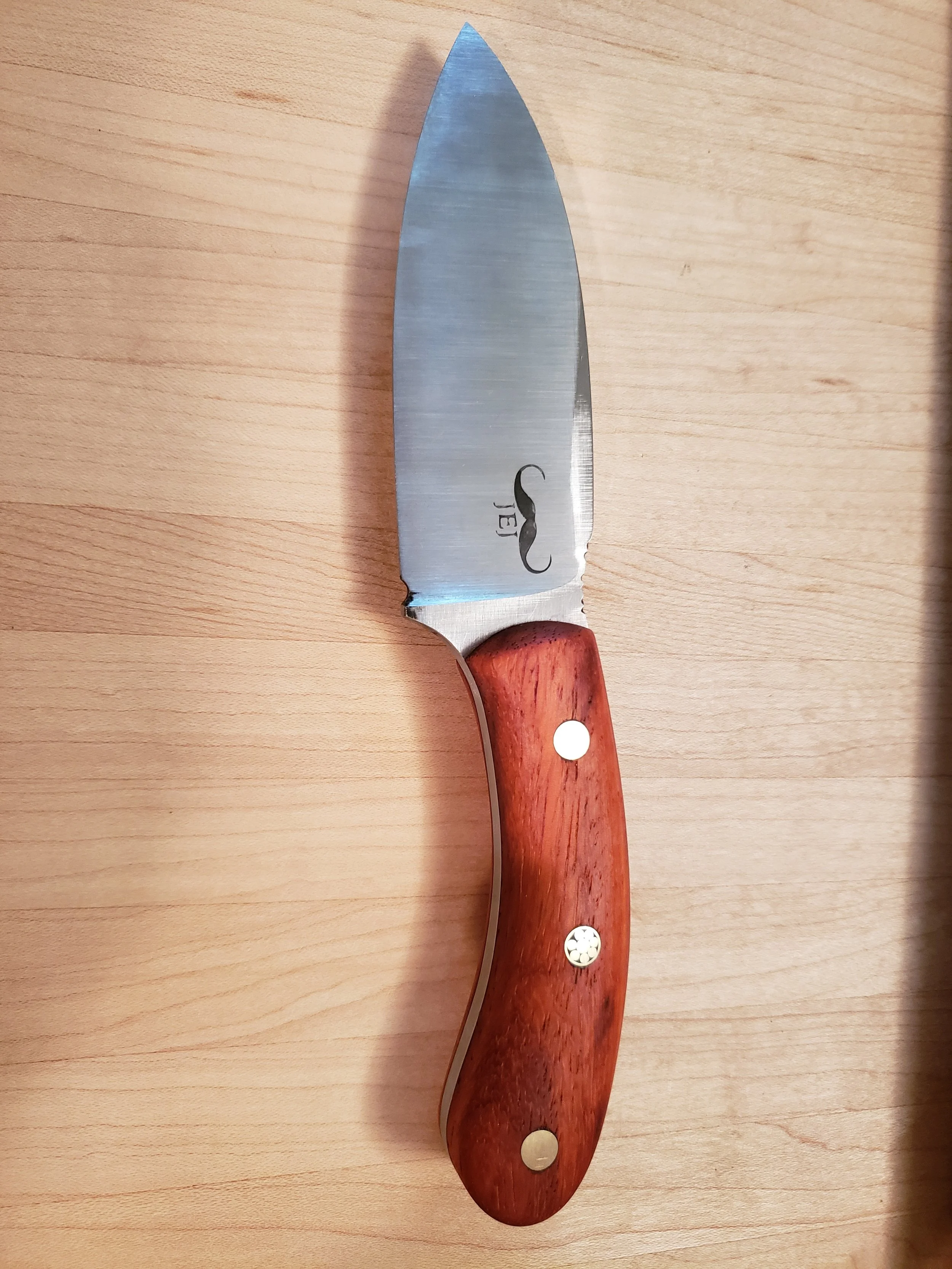 A stainless steel kitchen knife with a wooden handle resting on a wooden surface.