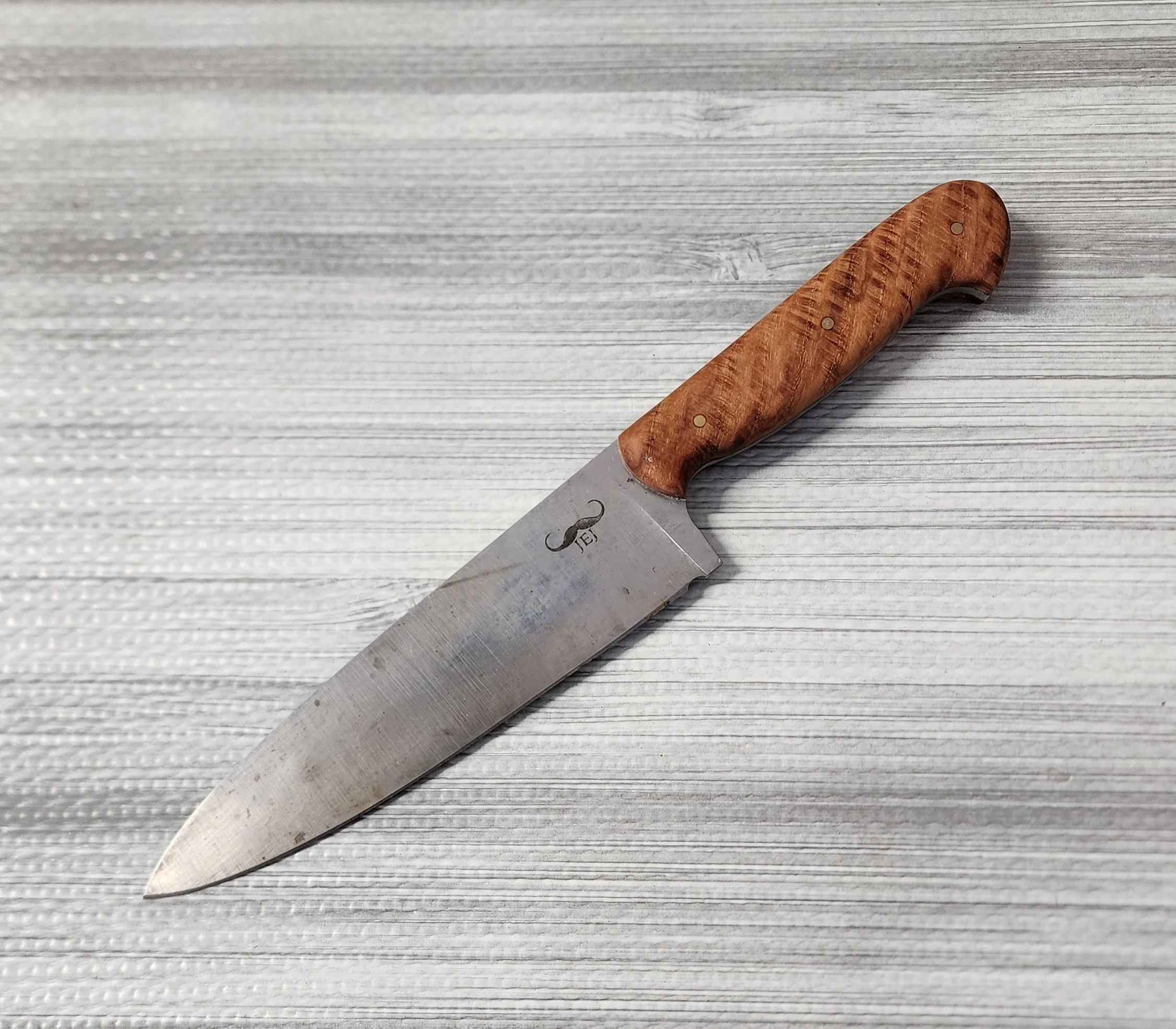 A fixed-blade kitchen knife with a wooden handle resting on a light-colored textured surface.