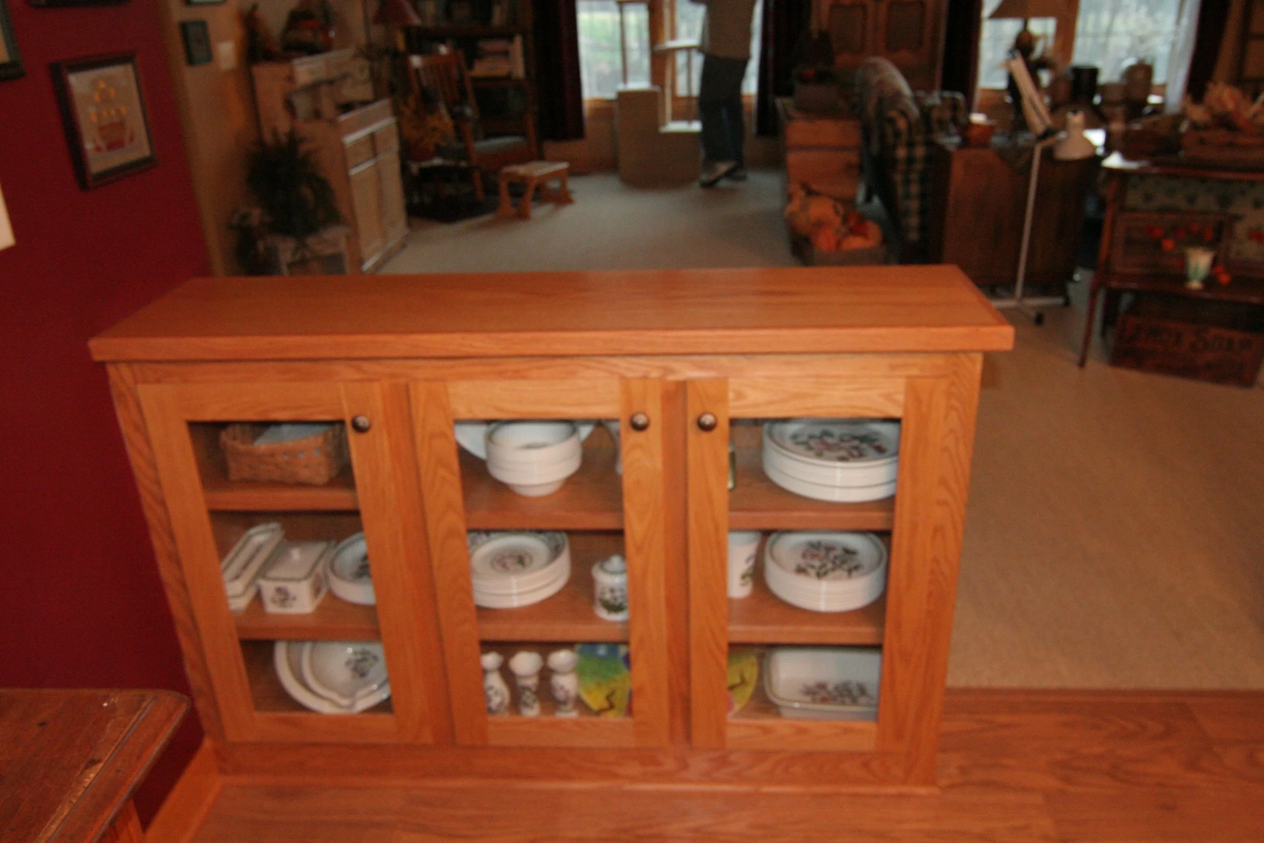Wooden china cabinet with glass doors displaying plates, bowls, and decorative items inside a cozy home.