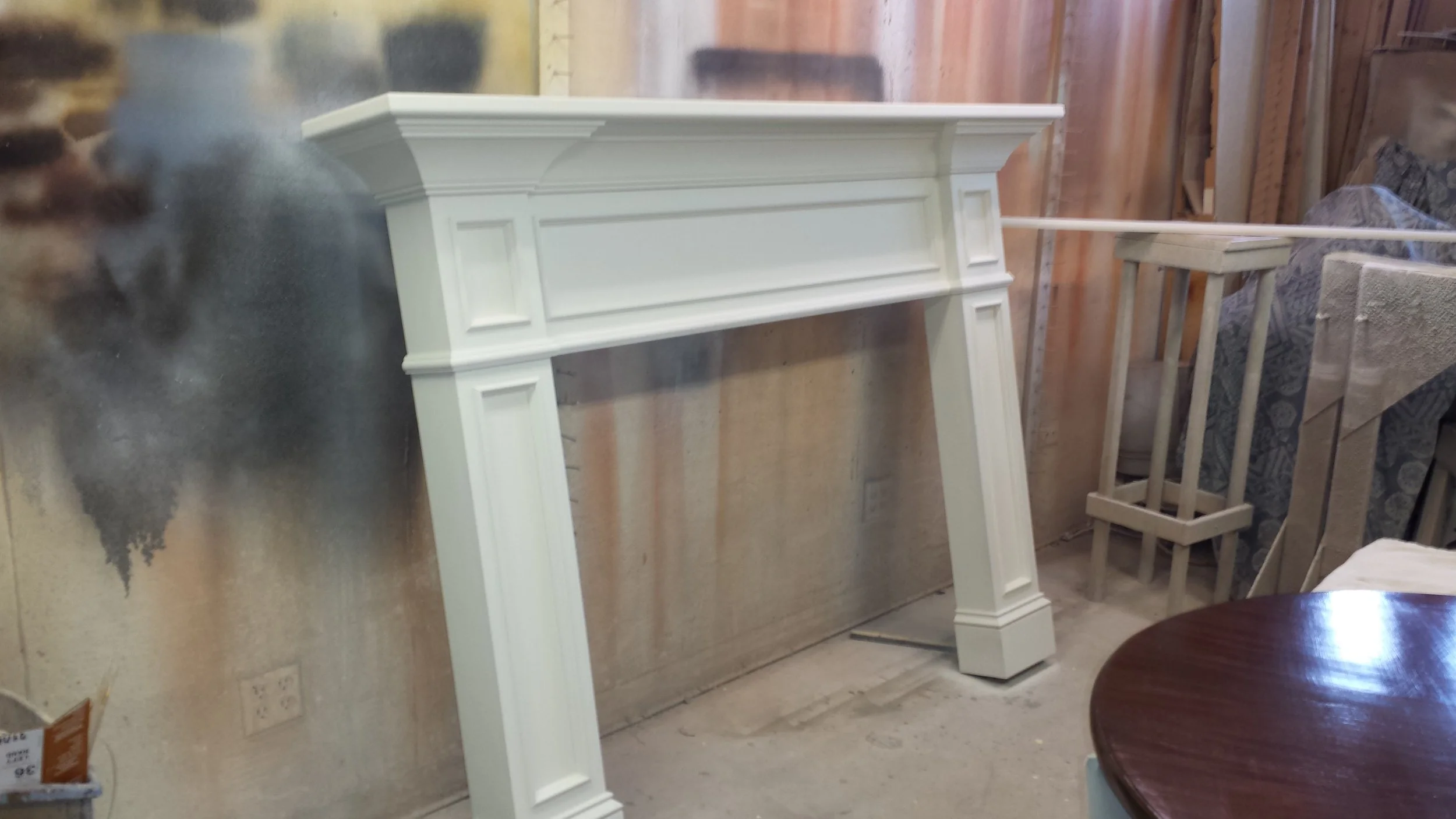 White wooden fireplace mantel in a workshop or furniture store setting.