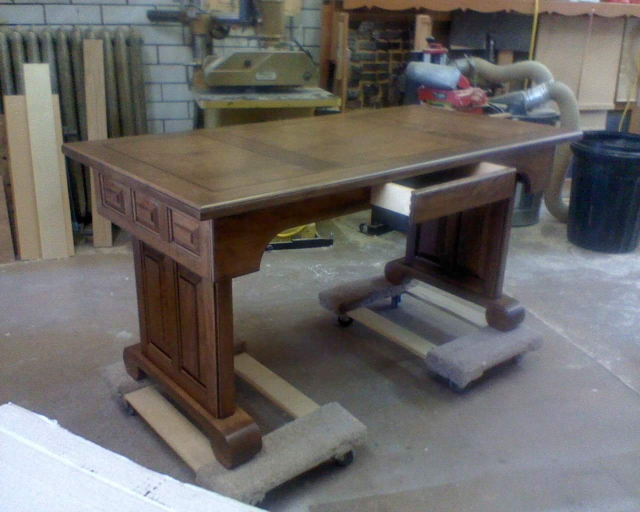 A wooden desk in a woodworking shop with tools and equipment in the background.