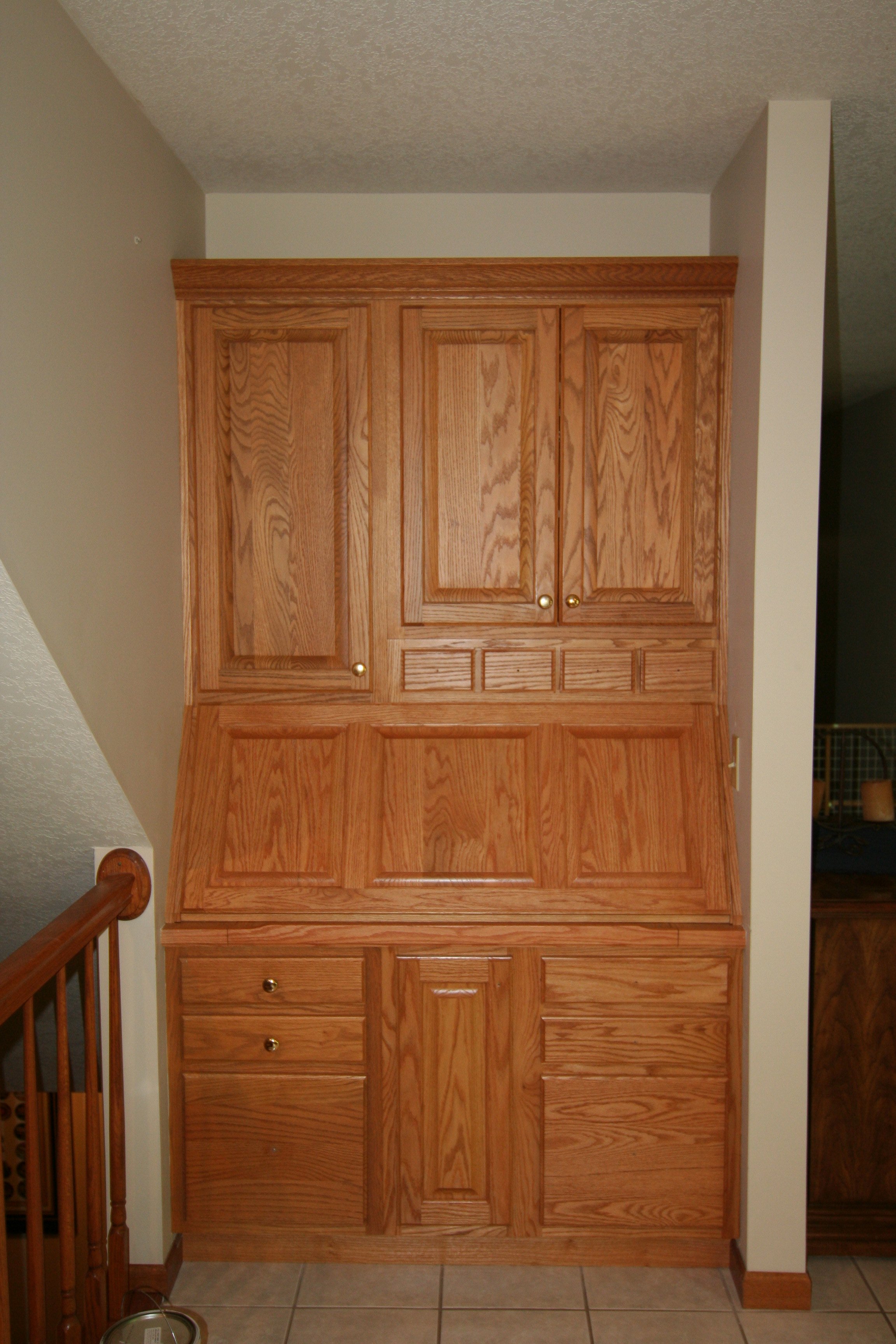 A tall wooden kitchen cabinet with upper and lower sections, featuring multiple drawers and doors, situated against a white wall in a home interior.