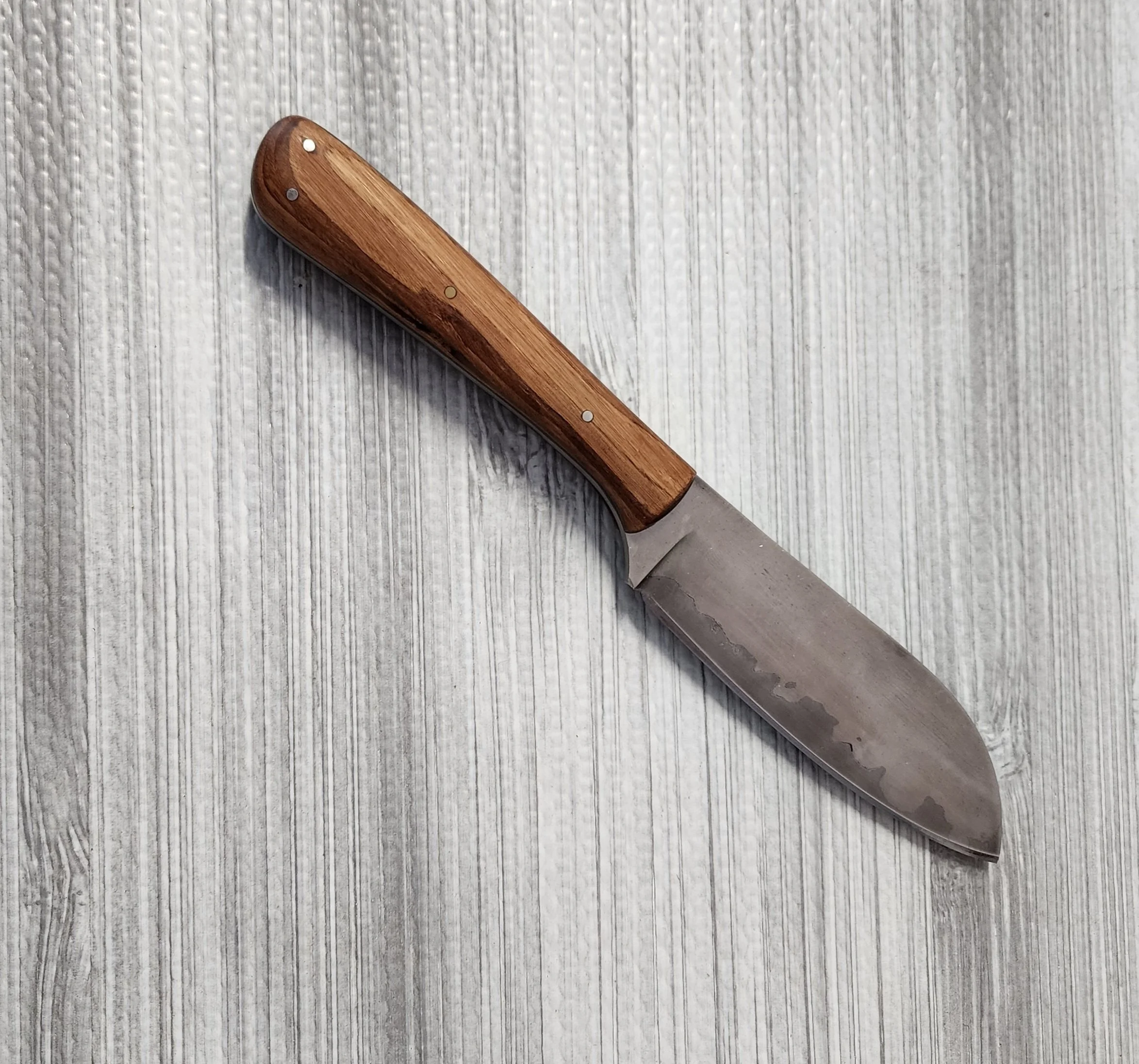 A stainless steel kitchen knife with a wooden handle resting on a gray wood-textured surface