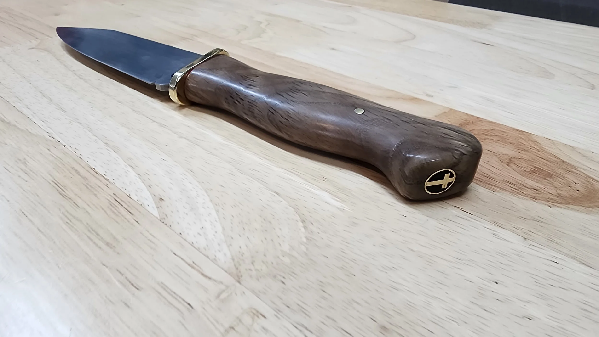 A pocket knife with a wooden handle, metal blade, and gold-colored accents placed on a light wooden surface.