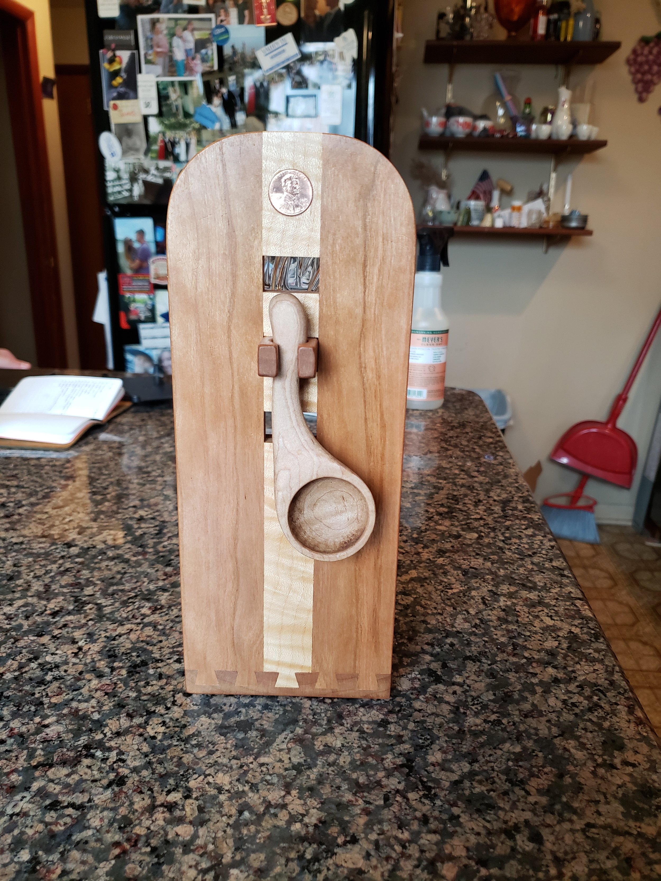 A wooden kitchen timer with a circular dial, mounted on a wooden stand, placed on a granite countertop in a kitchen.