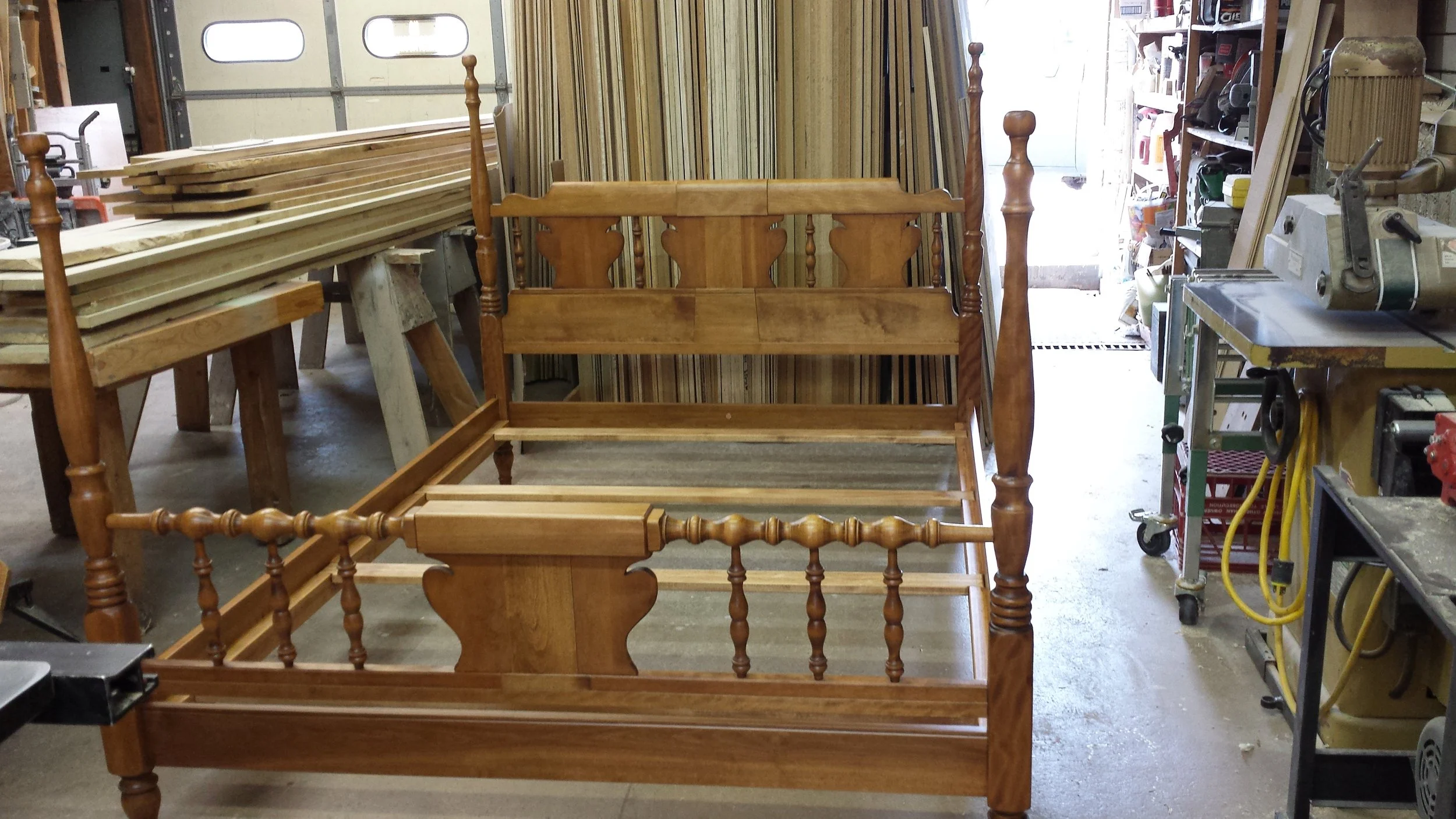 Wooden bed frame with headboard and footboard in a woodworking workshop.