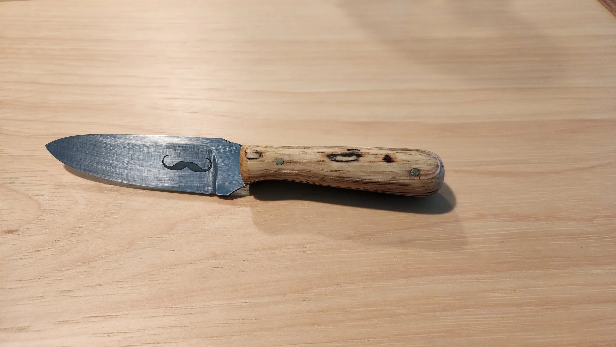 Small kitchen knife with a metal blade engraved with a mustache, and a handle made of wood.