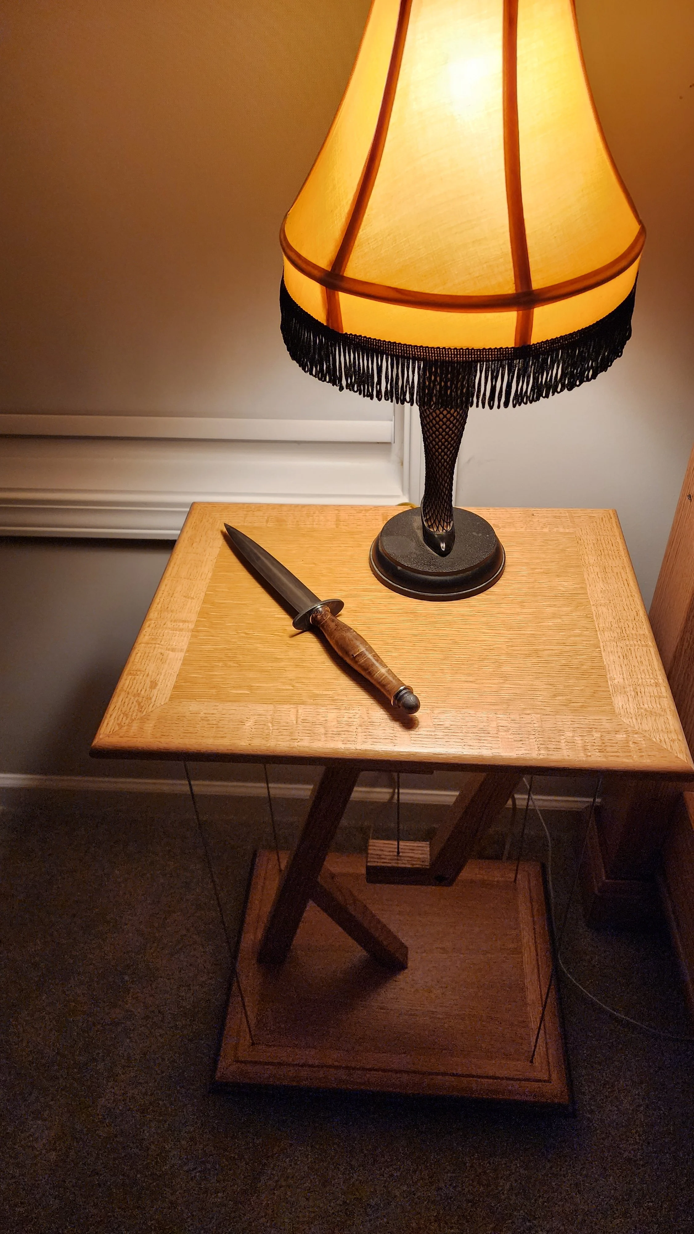 A wooden side table with a table lamp and a knife resting on it.