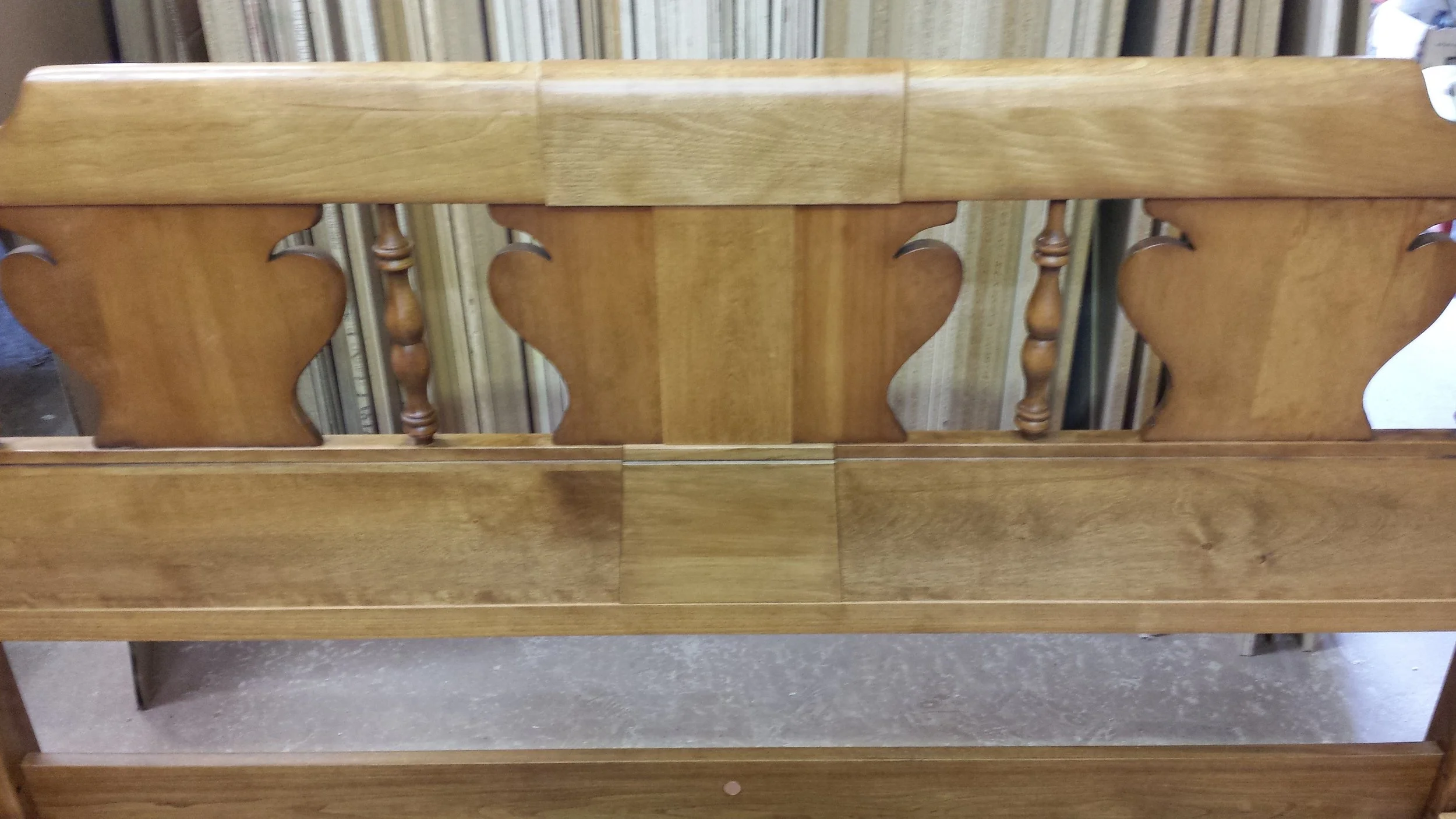 Front view of a wooden headboard with intricate cutout designs and vertical spindles, placed against a backdrop of vertically striped fabric.