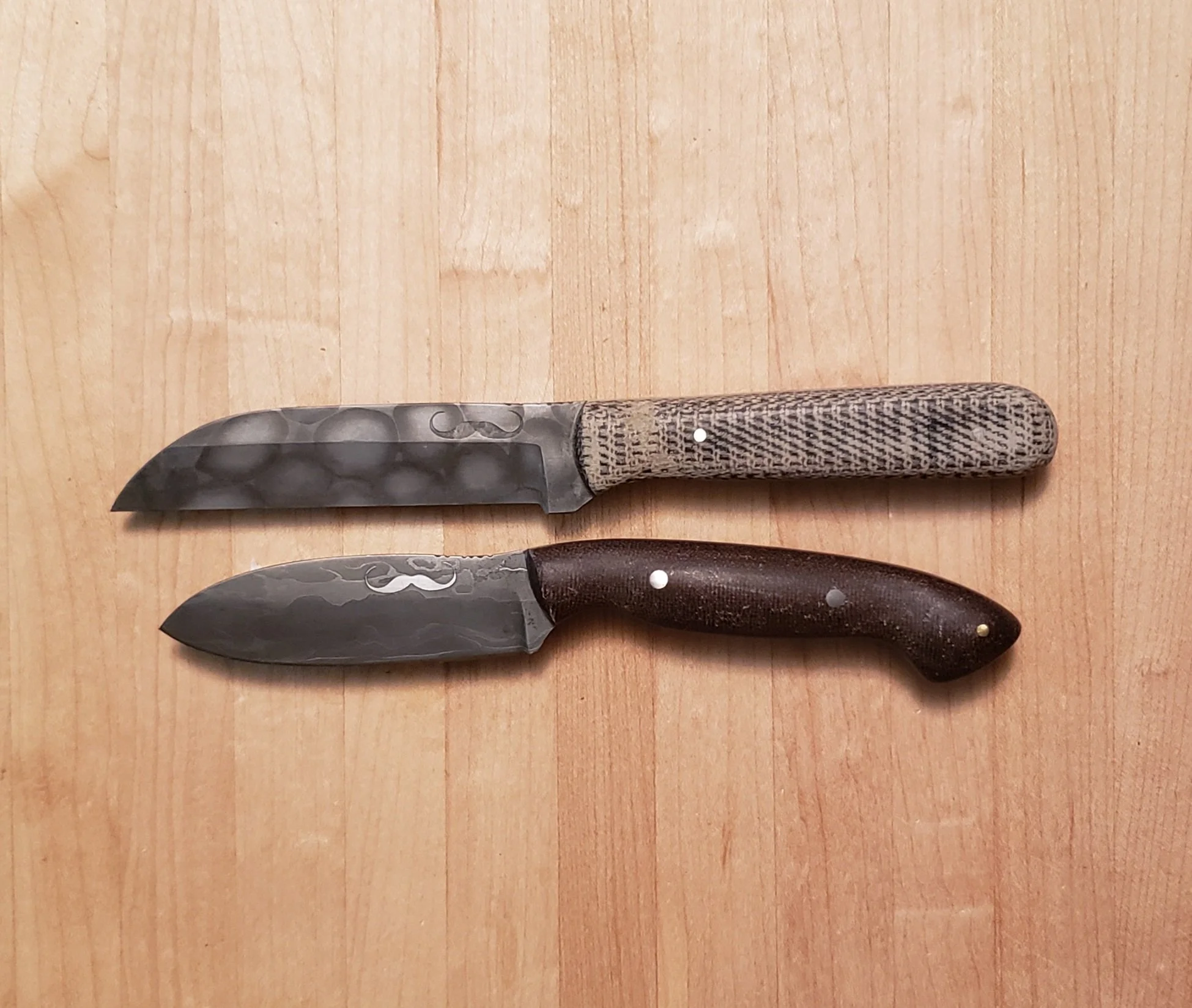 Two handcrafted knives with Damascus steel blades and textured wooden handles on a wooden surface.