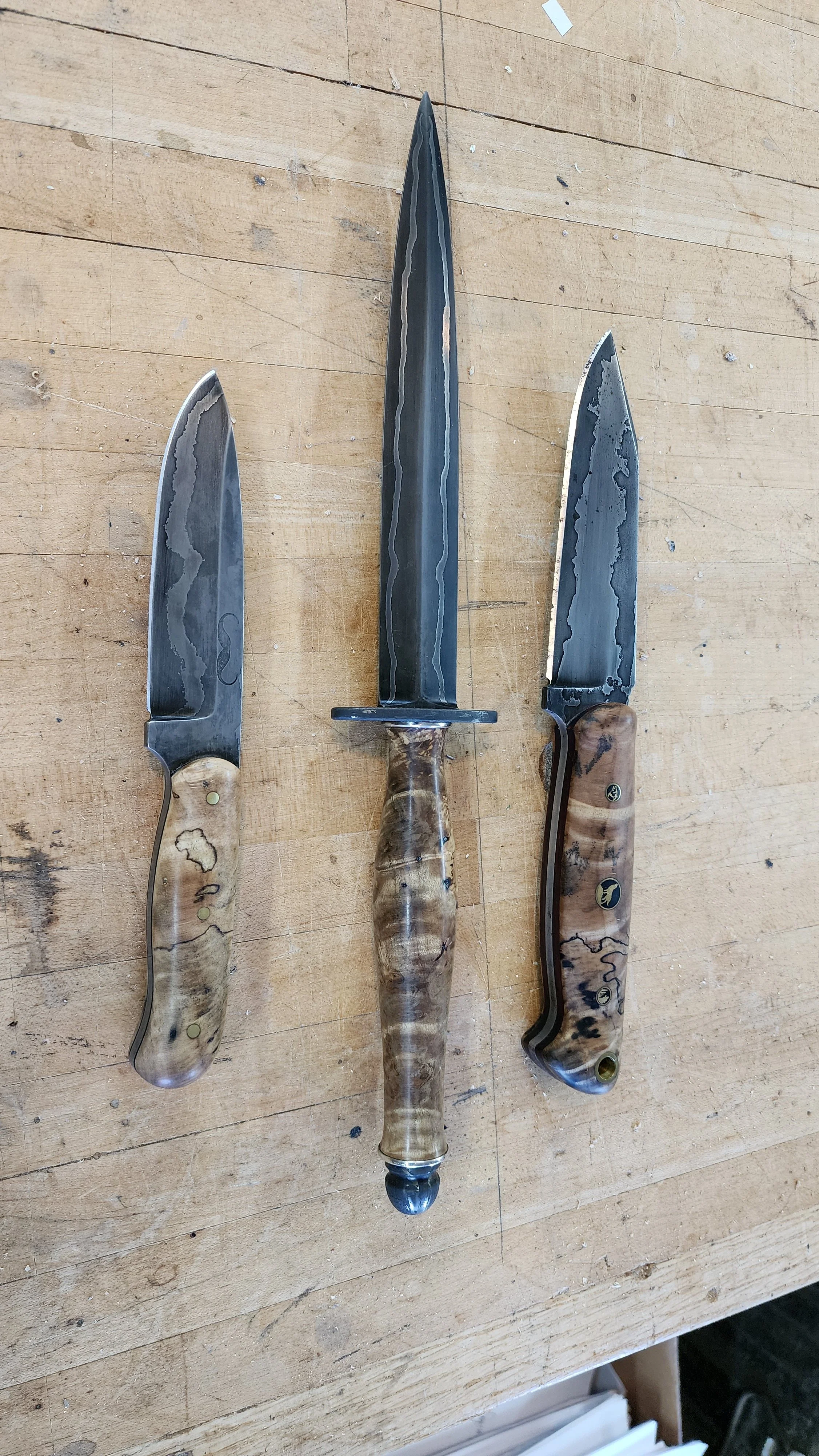 Three knives with wooden handles and patterned blades are placed on a wooden surface.