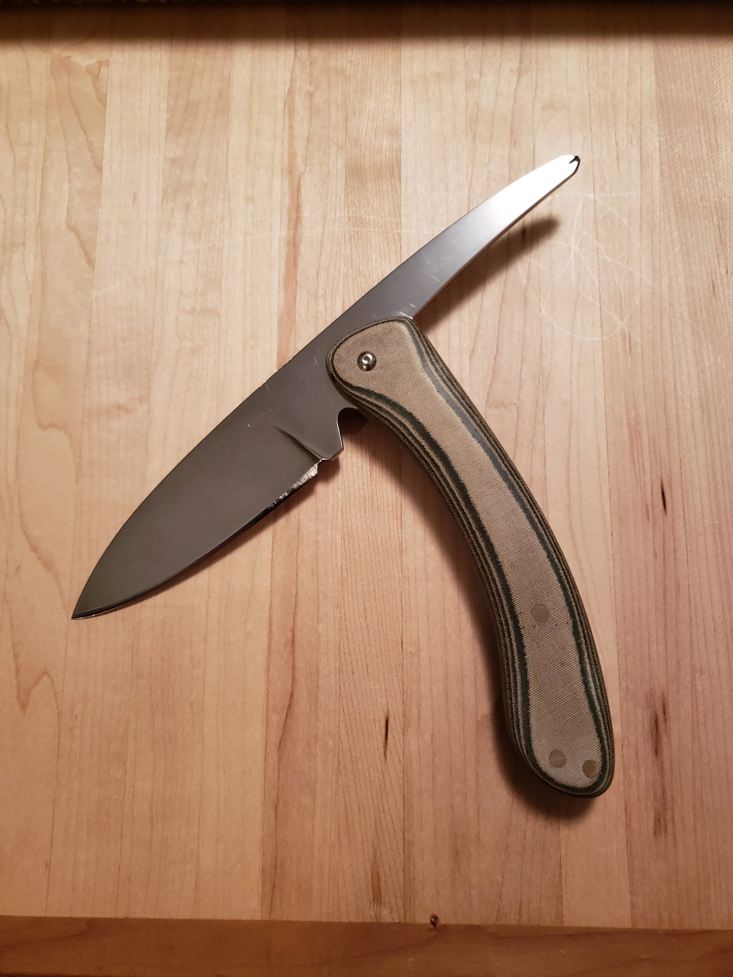 A folding pocket knife with a partially serrated black blade and a camouflage handle, open on a wooden surface.