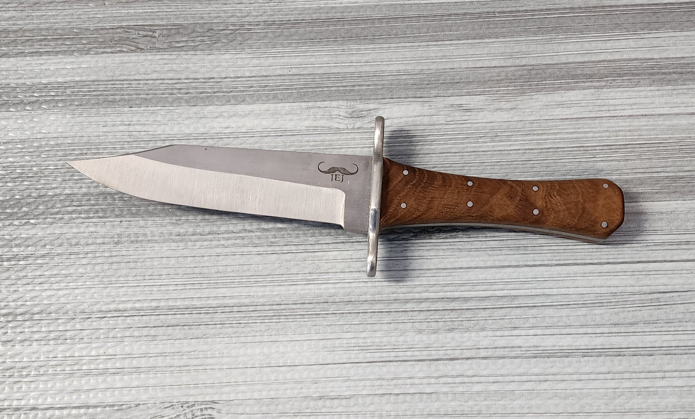 A knife with a stainless steel blade and a wooden handle on a textured light gray wooden surface.
