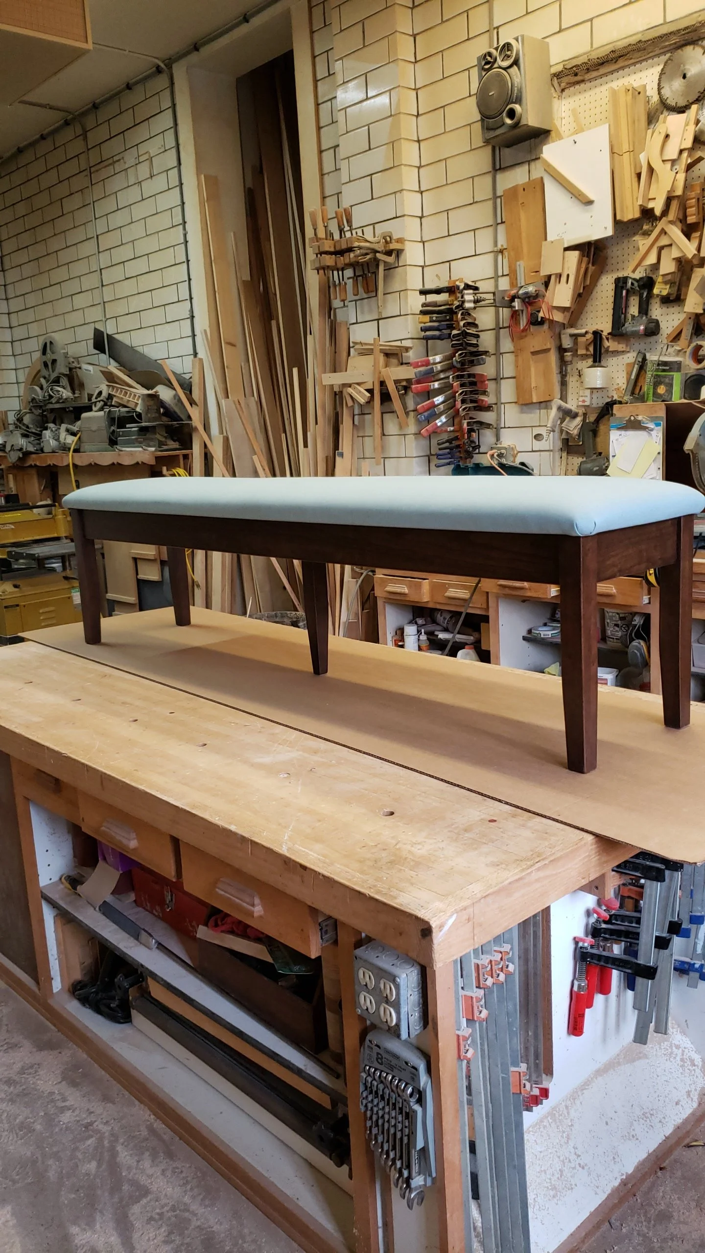 A sewing or ironing bench with a white cushioned top in a woodworking shop.