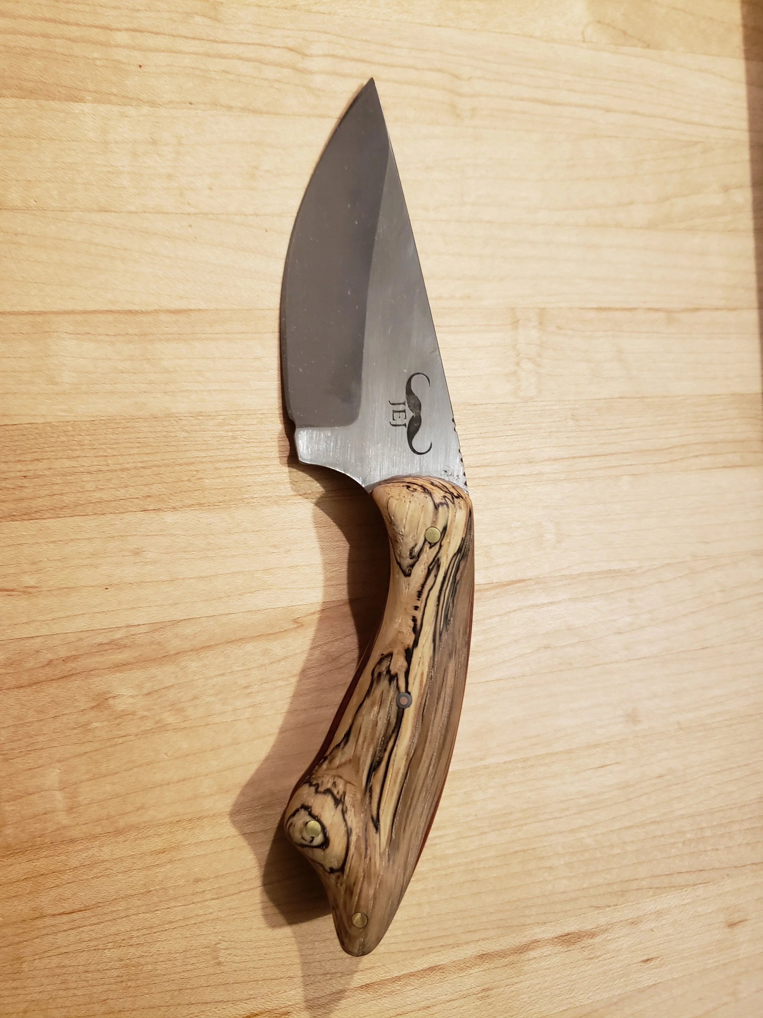 A folding pocket knife with a steel blade and a wooden handle resting on a wooden surface.