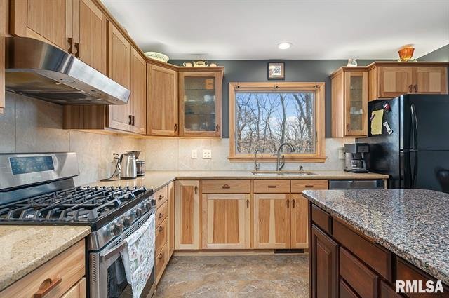 Kitchen with wooden cabinets, a black refrigerator, a gas stove, a coffee maker, a coffee pot, and a window showing trees outside.