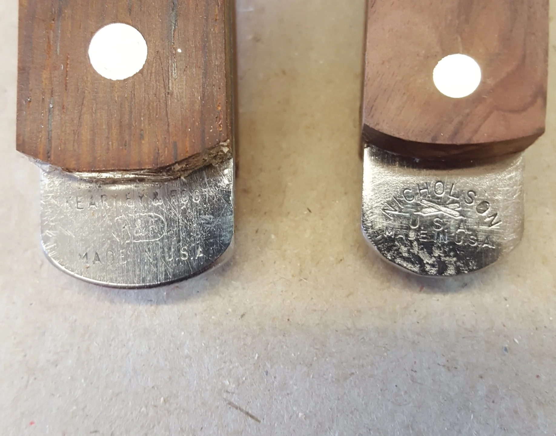Close-up of two woodworking chisels with wooden handles and metal blades, resting on a surface. The blades are stamped with brand names and origin details.
