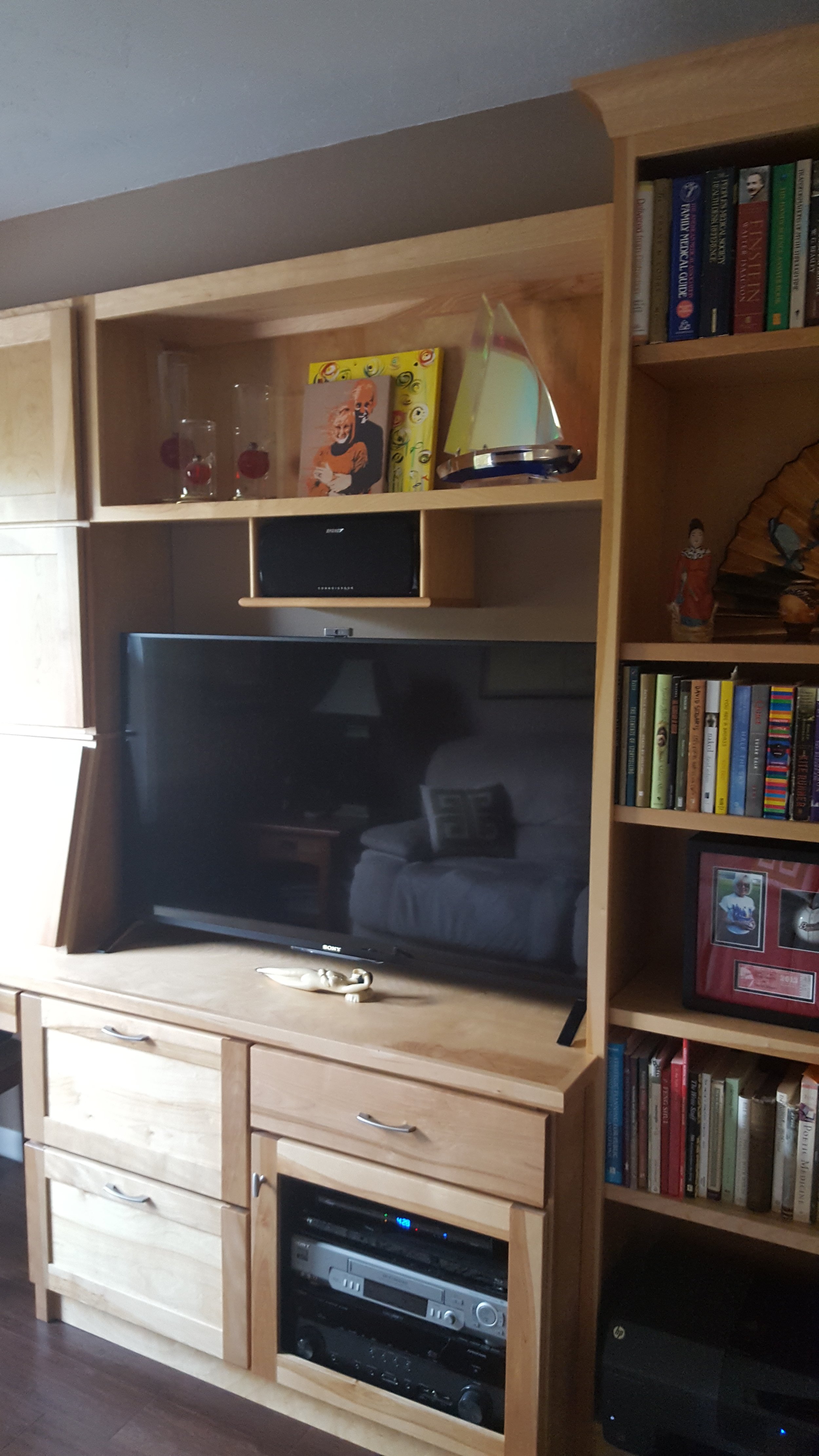 A wooden entertainment center with a flat-screen TV, books, decorative items, and electronic equipment.