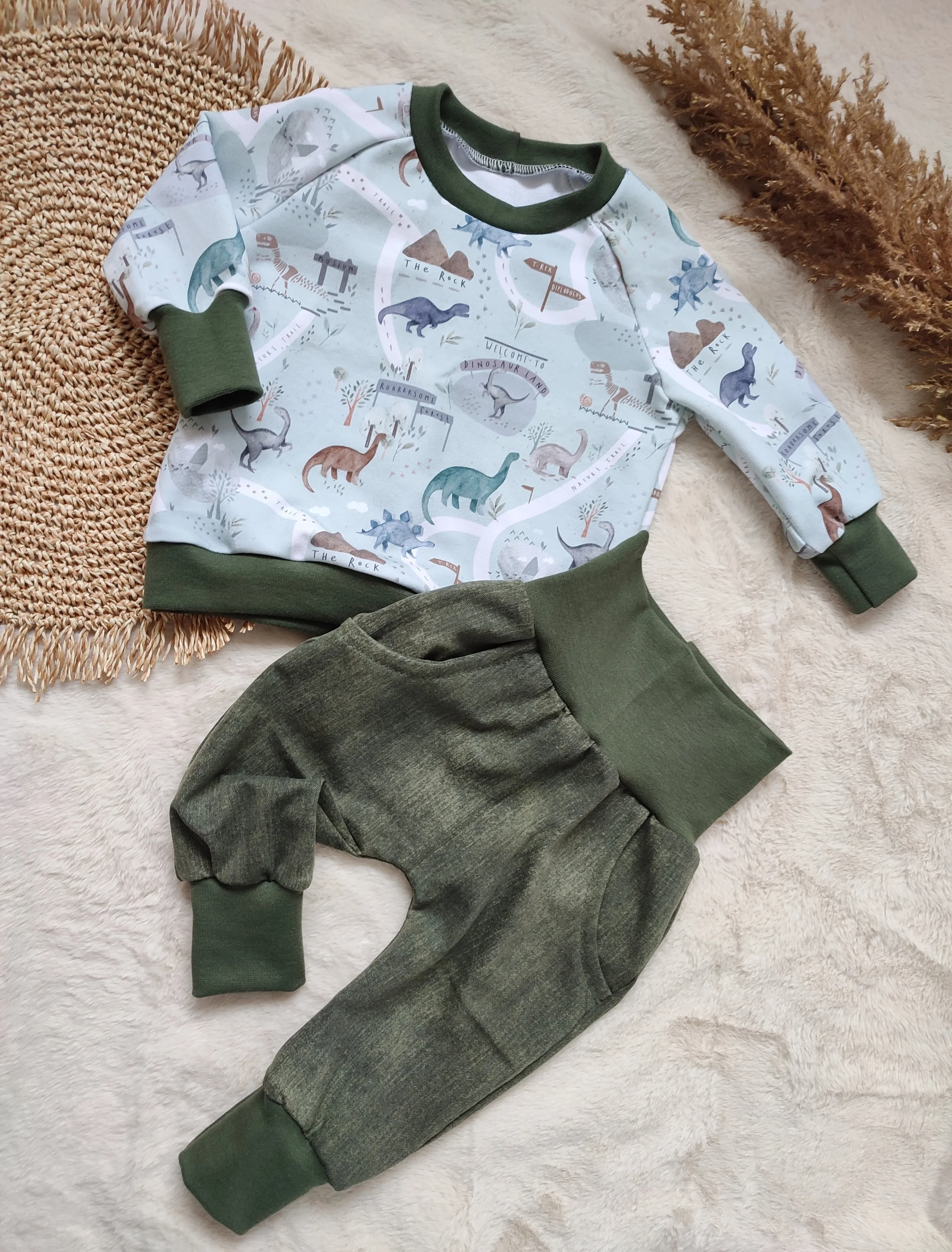 Kinderpyjama mit Dinosaurier-Motiven, grünem Kragen und Bündchen, auf weichem, cremefarbenem Untergrund