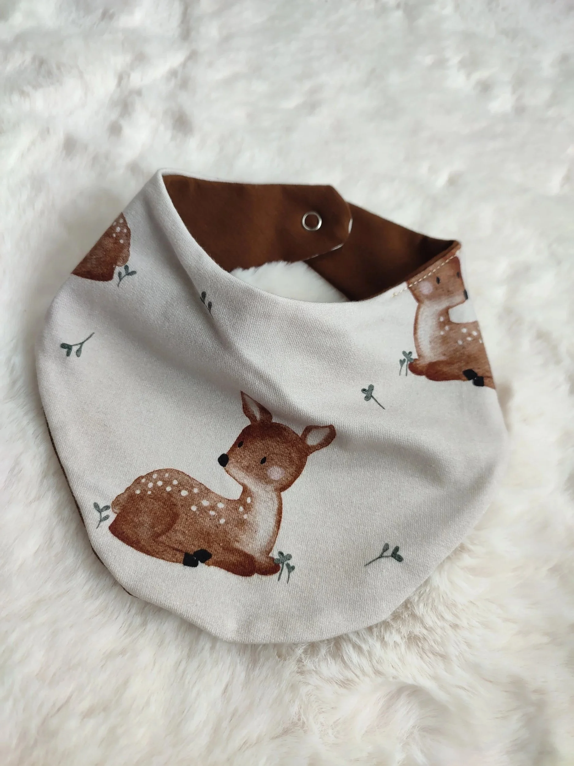Baby Halstuch mit braunem Rand und Reh-Design auf weißem Hintergrund, liegt auf Fellunterlage.