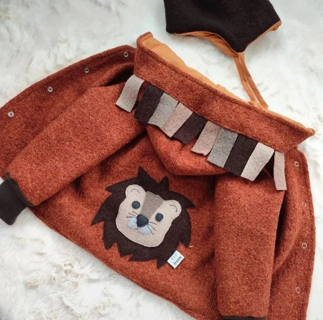 Ein roter Pullover mit einem Löwenmuster auf der Brust, eine warme Mütze und eine Flasche auf einem weißen Fellteppich