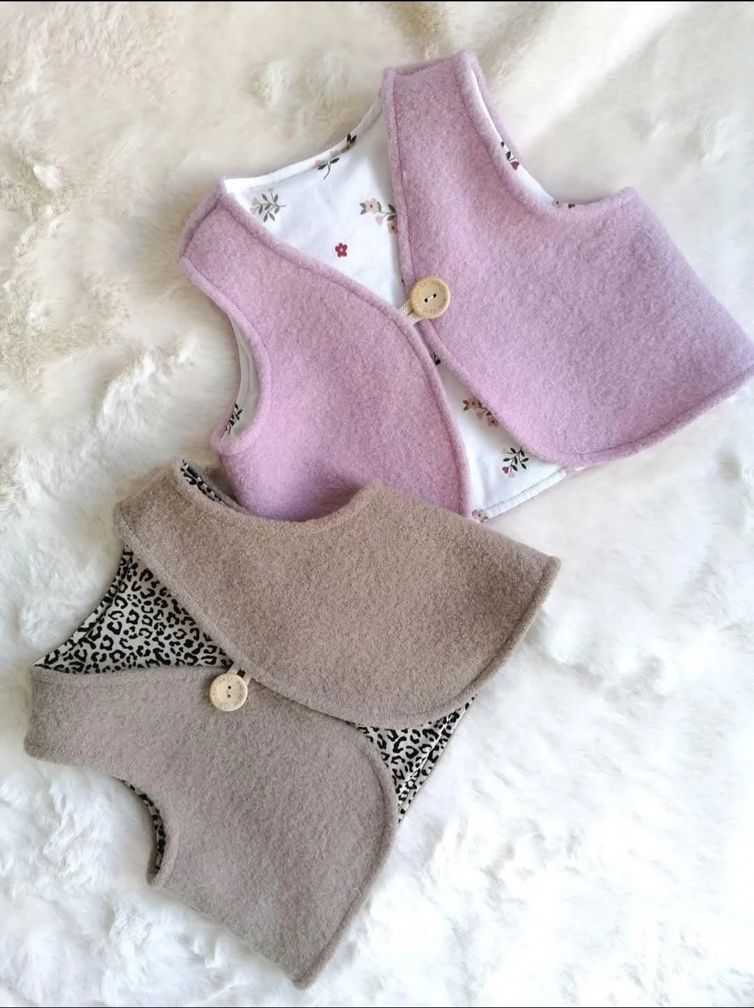 Zwei samtene Kinderhalstücher, eines pink mit floralem Muster und eines beige mit Leo-Muster, auf weißem, flauschigem Hintergrund.