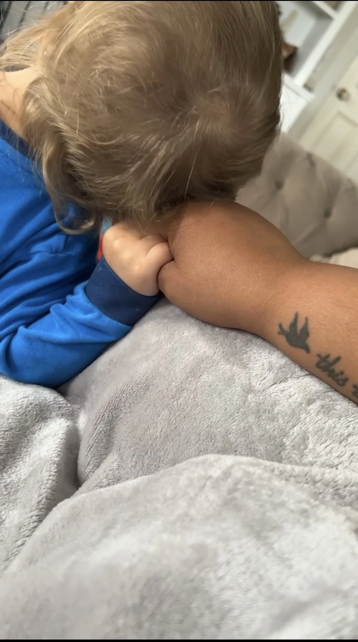 A child with blond hair resting their head on a person's arm, which has a tattoo of a bird and the words 'the bird' on the forearm.