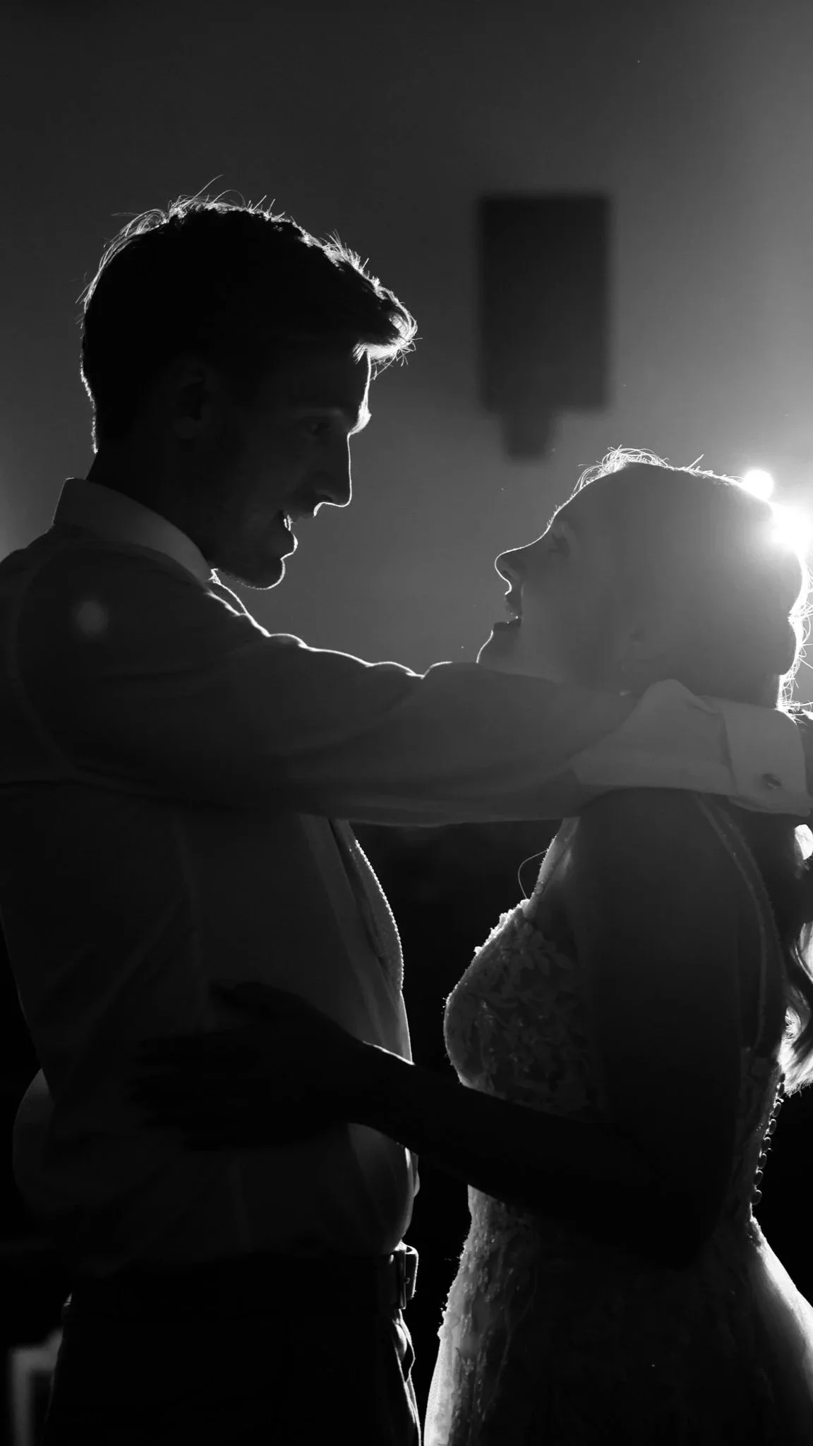 Ein schwarzer und weißer Silhouetten-Couple tanzt zusammen, die Frau trägt ein Kleid mit Spitzen, das männliche Part trägt eine Hemd, im Hintergrund Lichtquelle.