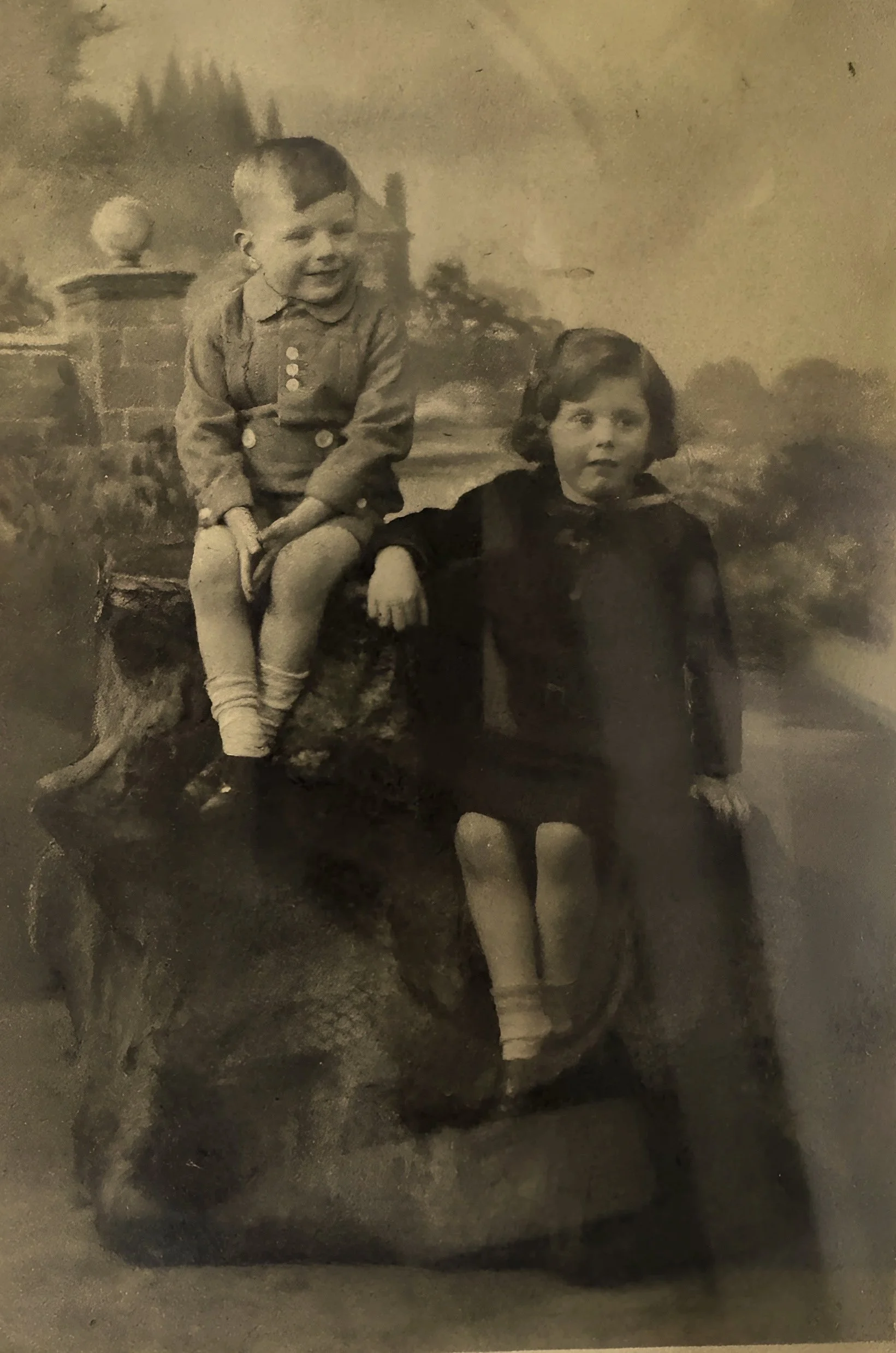 Two children, a boy and a girl, sitting on a large animal sculpture in an indoor setting with a painted background.