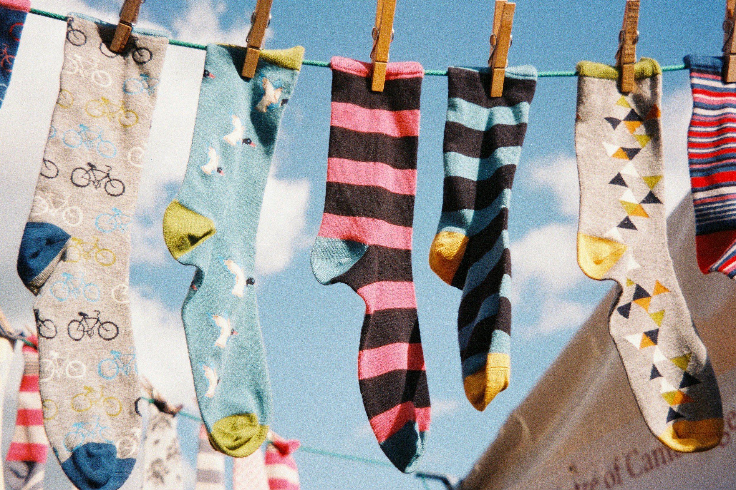 Colorful socks hanging on a clothesline outdoors against a blue sky with clouds.